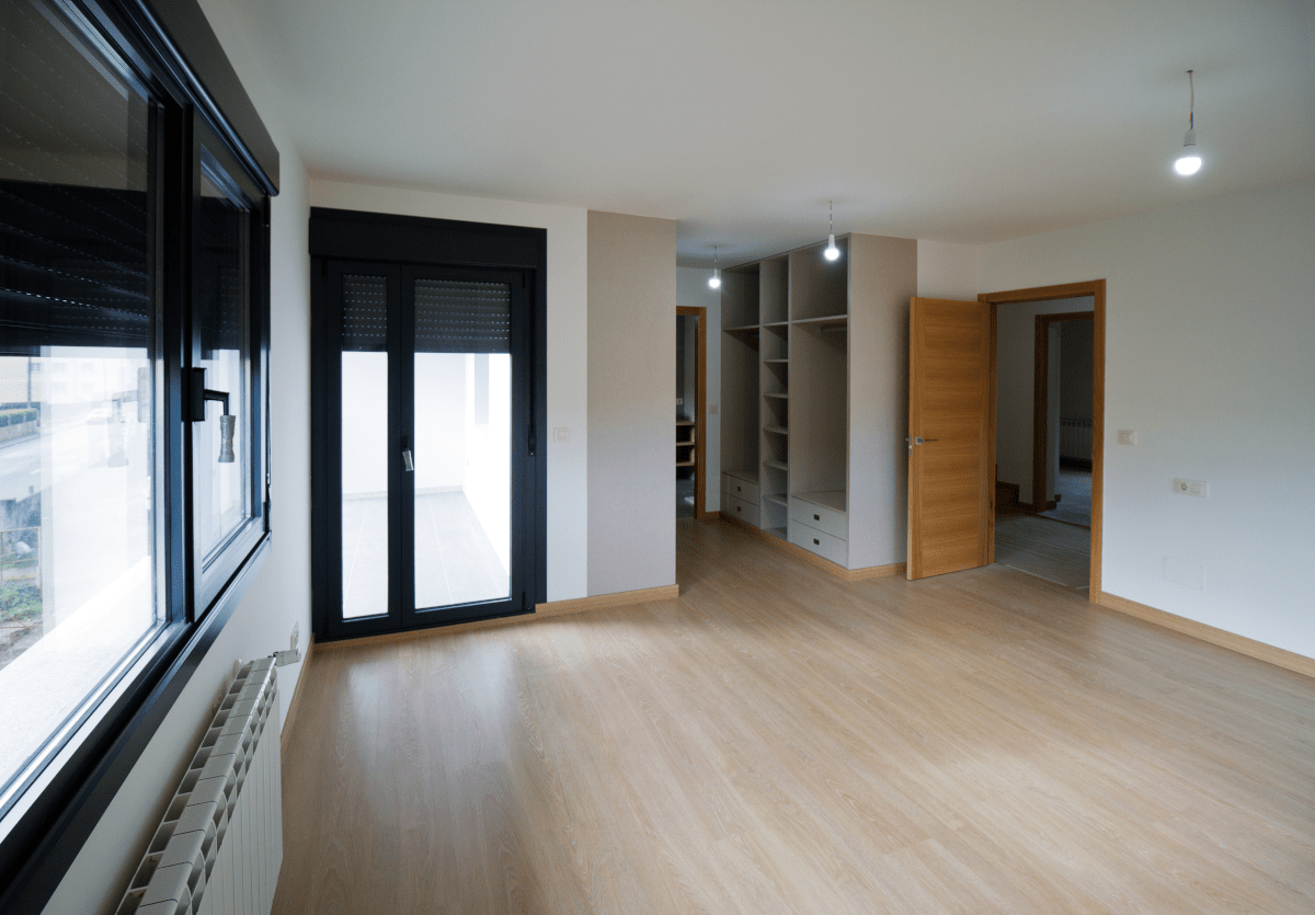 Una habitación vacía con pisos de madera y dos ventanas.