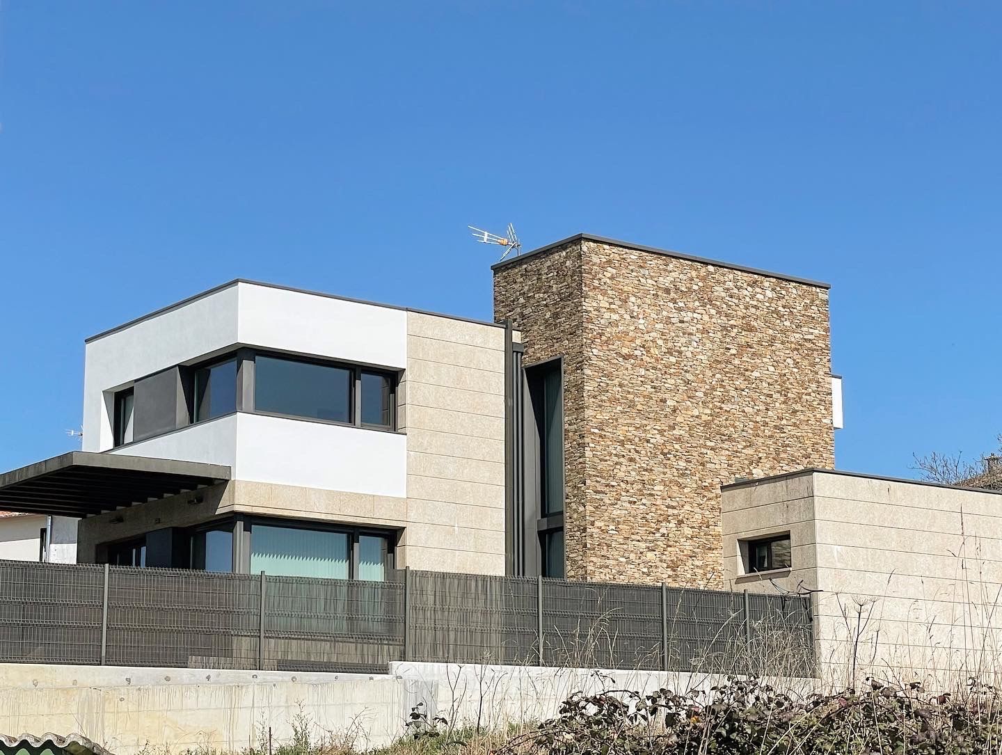 Una casa moderna con una valla alrededor y un cielo azul al fondo.