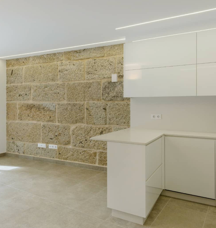 Una cocina con pared de piedra y gabinetes blancos.