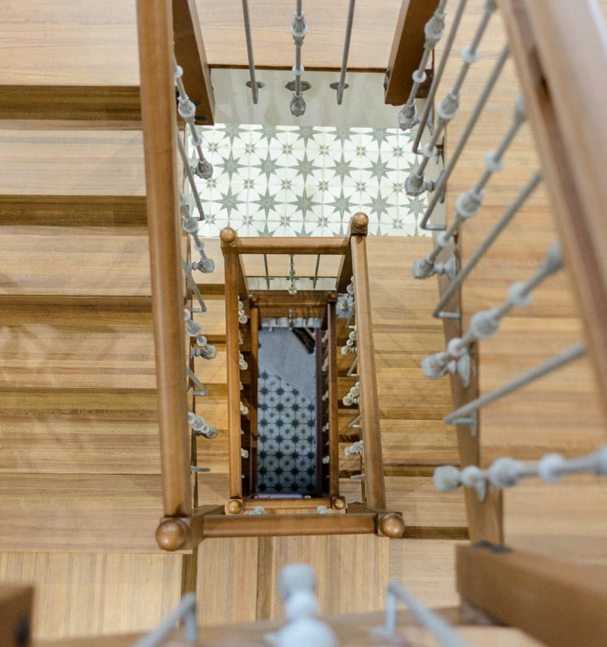 Mirando hacia abajo por una escalera de madera con barandilla de metal.
