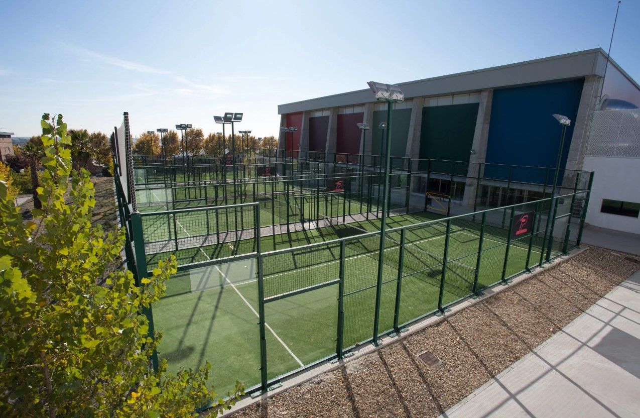 Una cancha de tenis con una valla alrededor y un edificio al fondo.