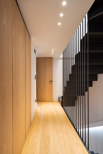 Un pasillo con suelo de madera y una escalera negra.