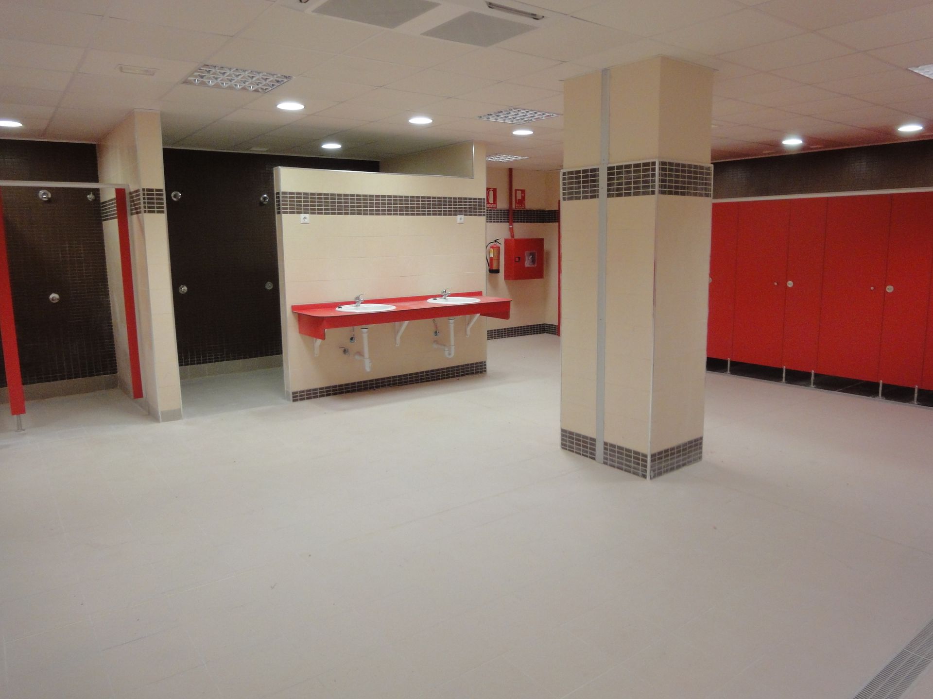Un baño vacío con cubículos y lavabos rojos.