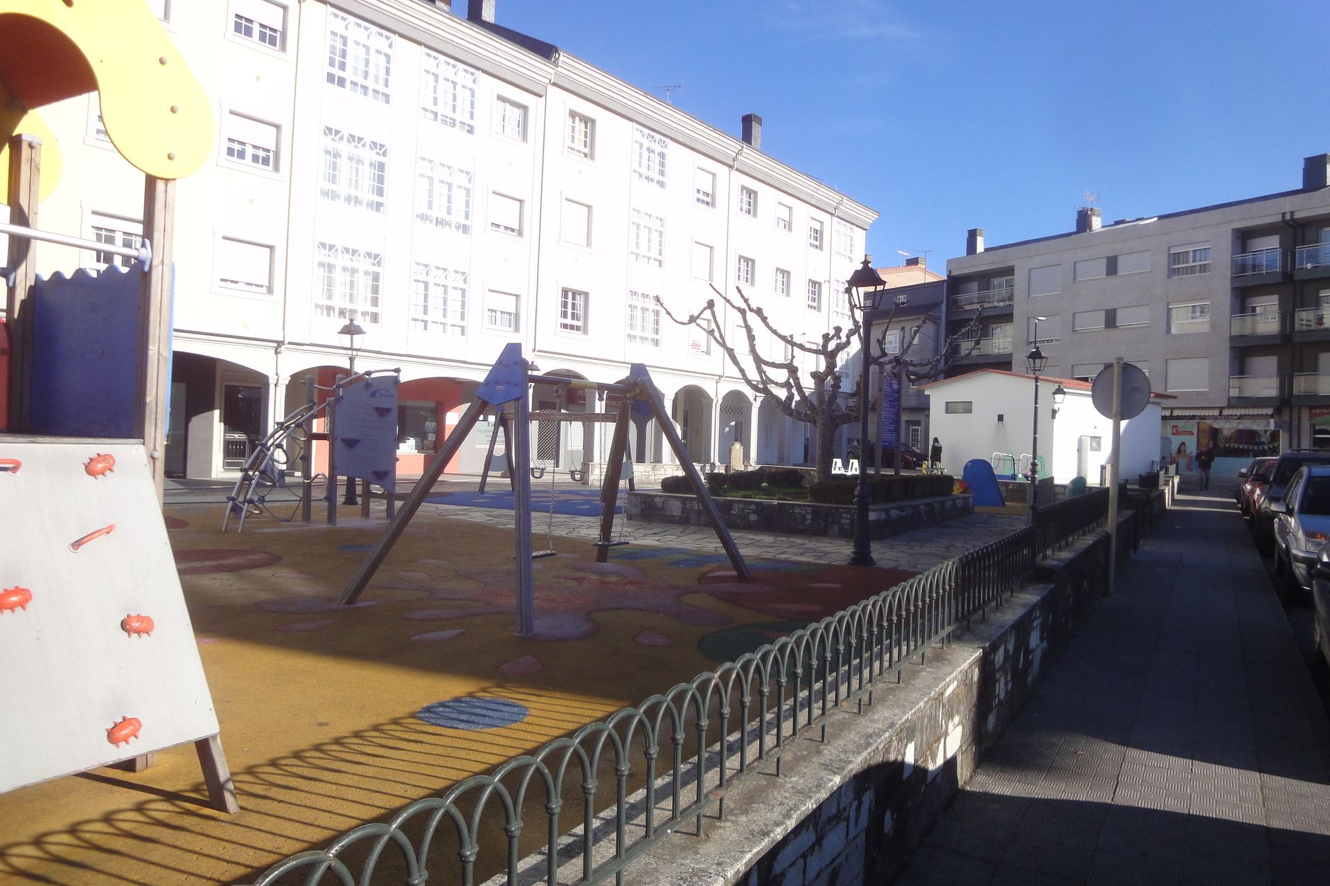 Un parque infantil frente a un edificio con coches aparcados delante.