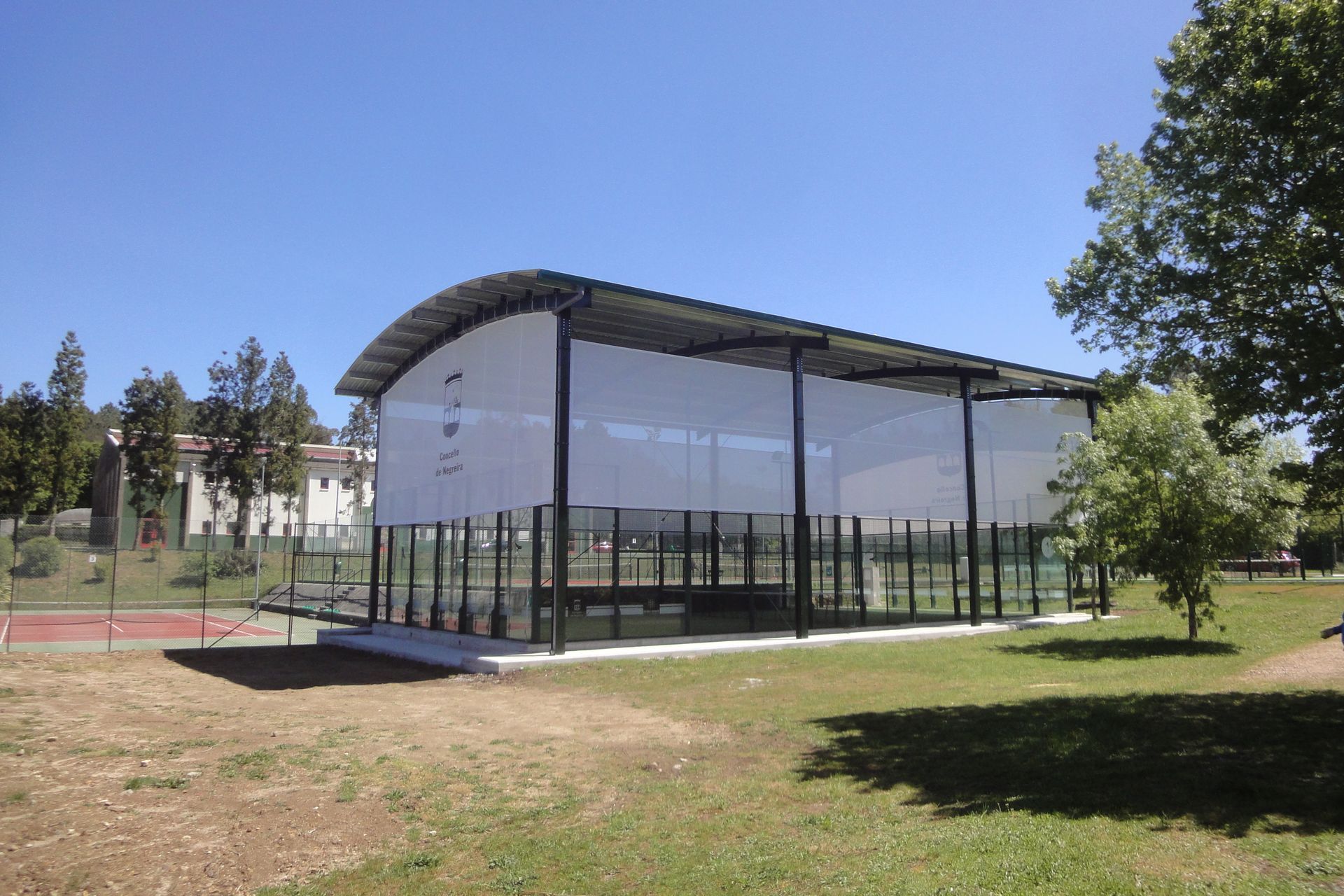 Un gran edificio con techo transparente está rodeado de césped y árboles.