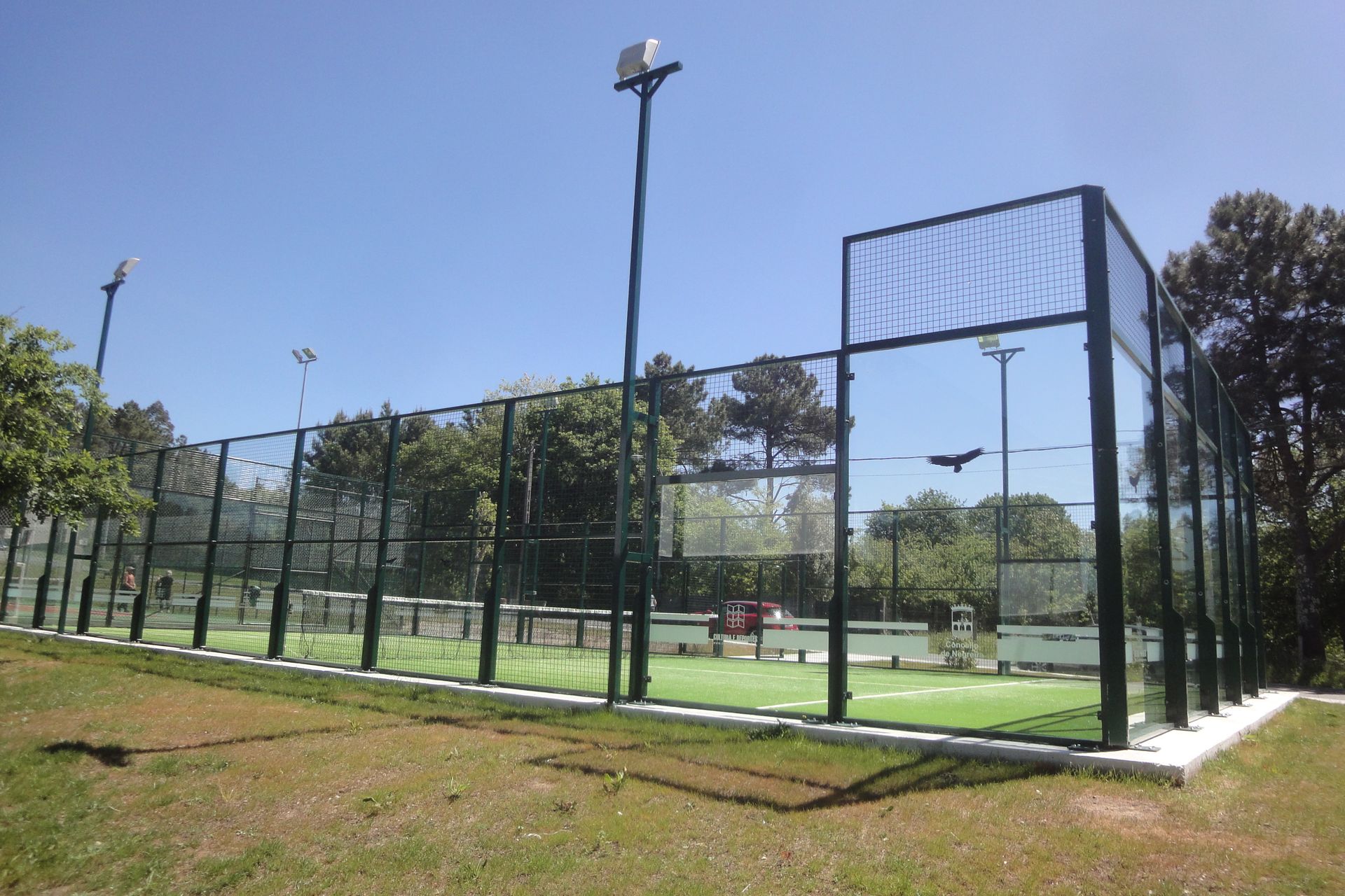 Una cancha de tenis con una valla alrededor y árboles al fondo.