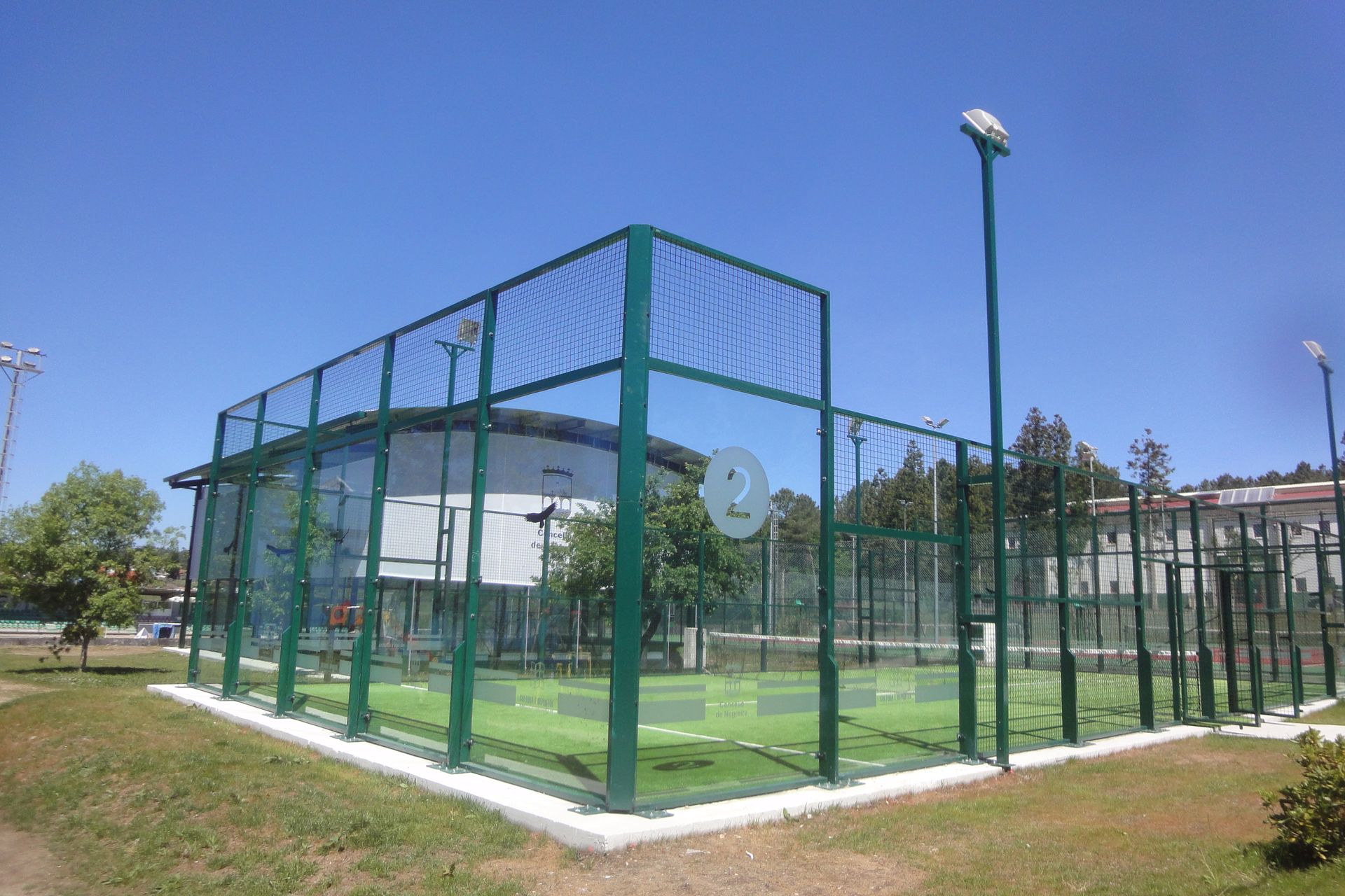 Una valla verde rodea una pista de pádel en un parque