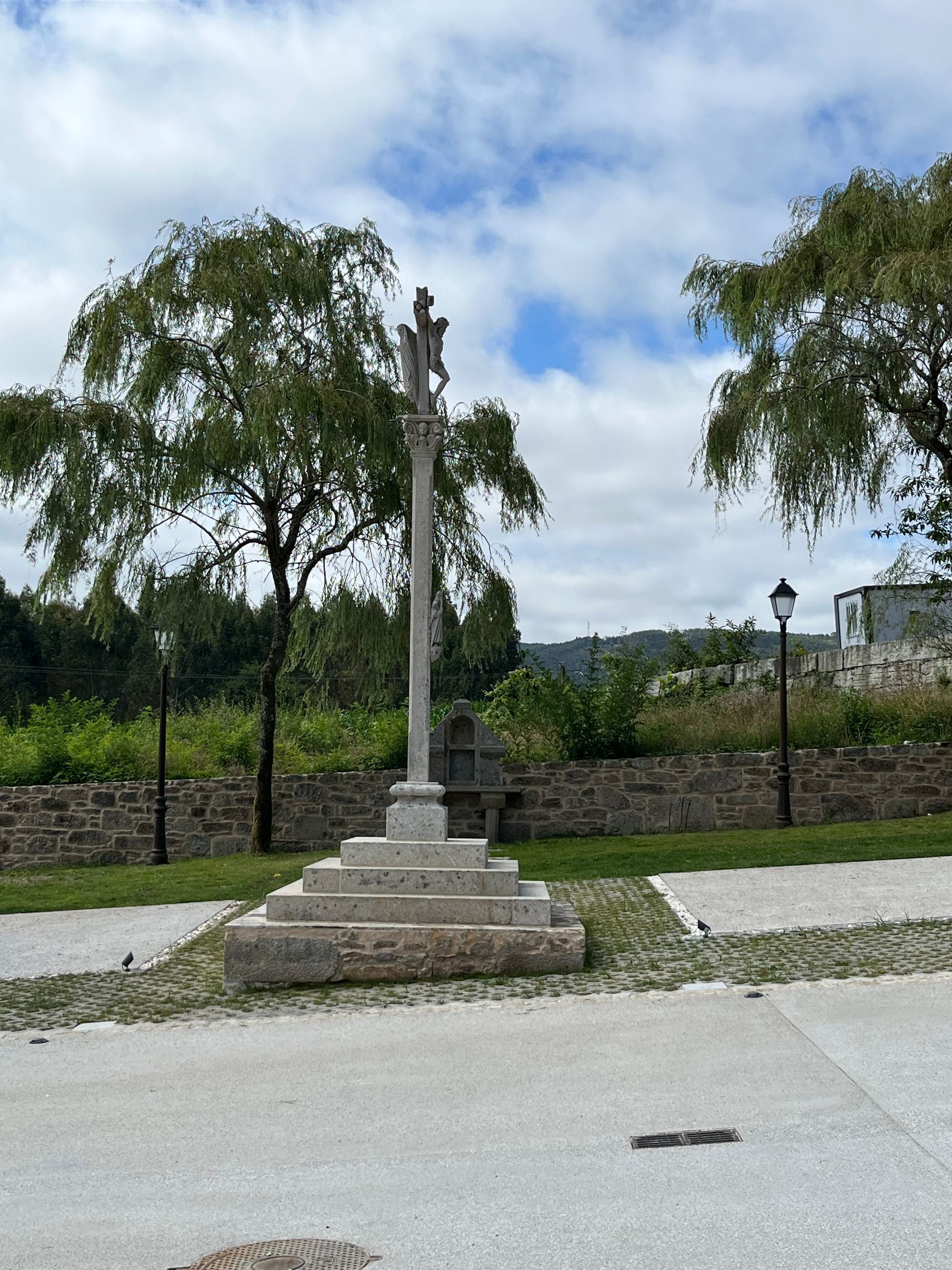 Una cruz de piedra en un parque con árboles al fondo.