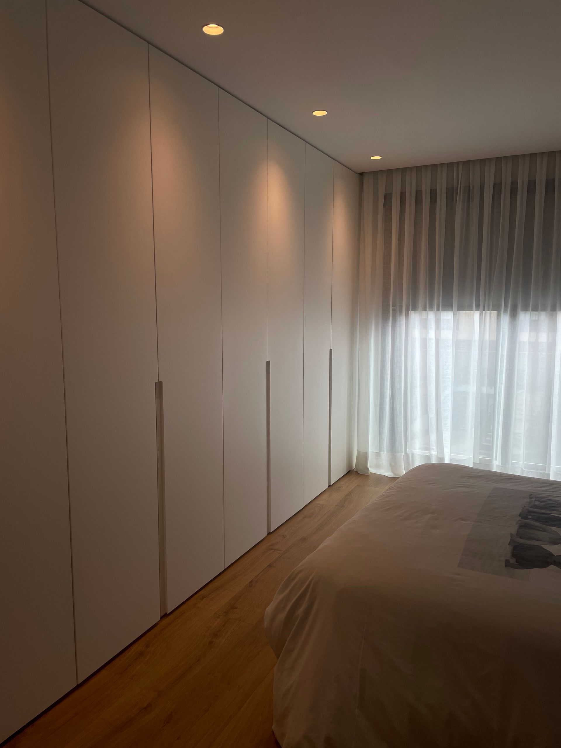 Un dormitorio con una cama y una ventana con cortinas blancas.