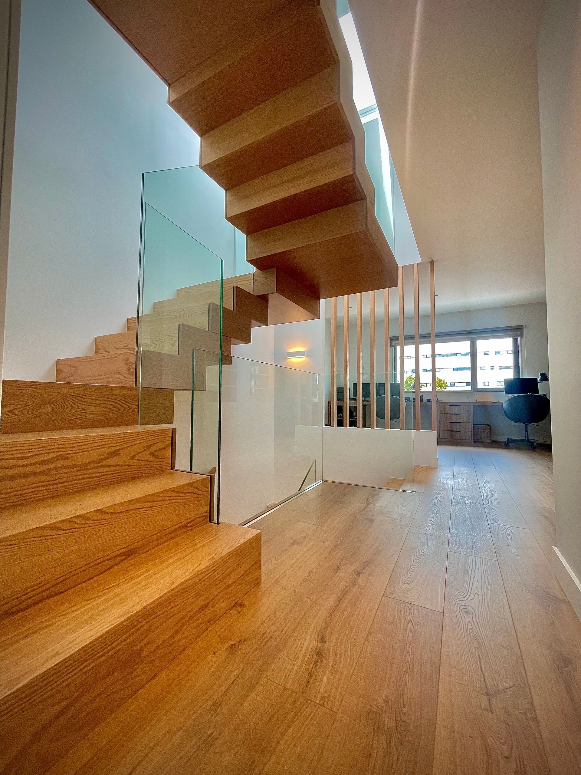 Una escalera de madera con barandilla de cristal en un pasillo.