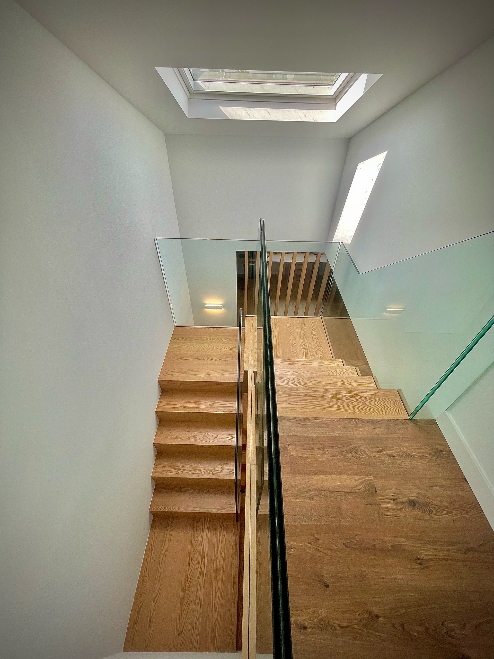 Una escalera con barandilla de cristal y una claraboya encima.