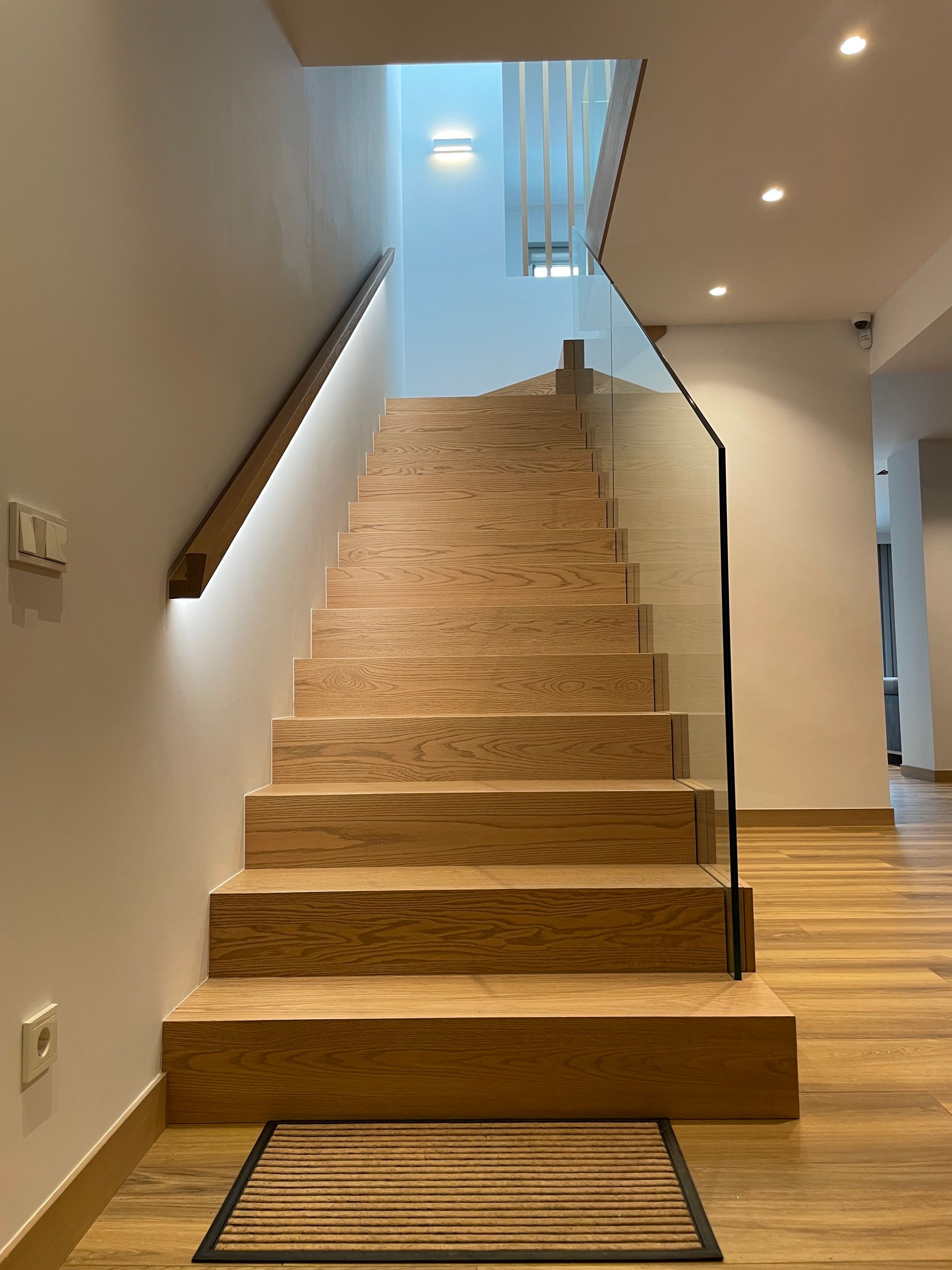 Una escalera con escalones de madera y barandilla de cristal.