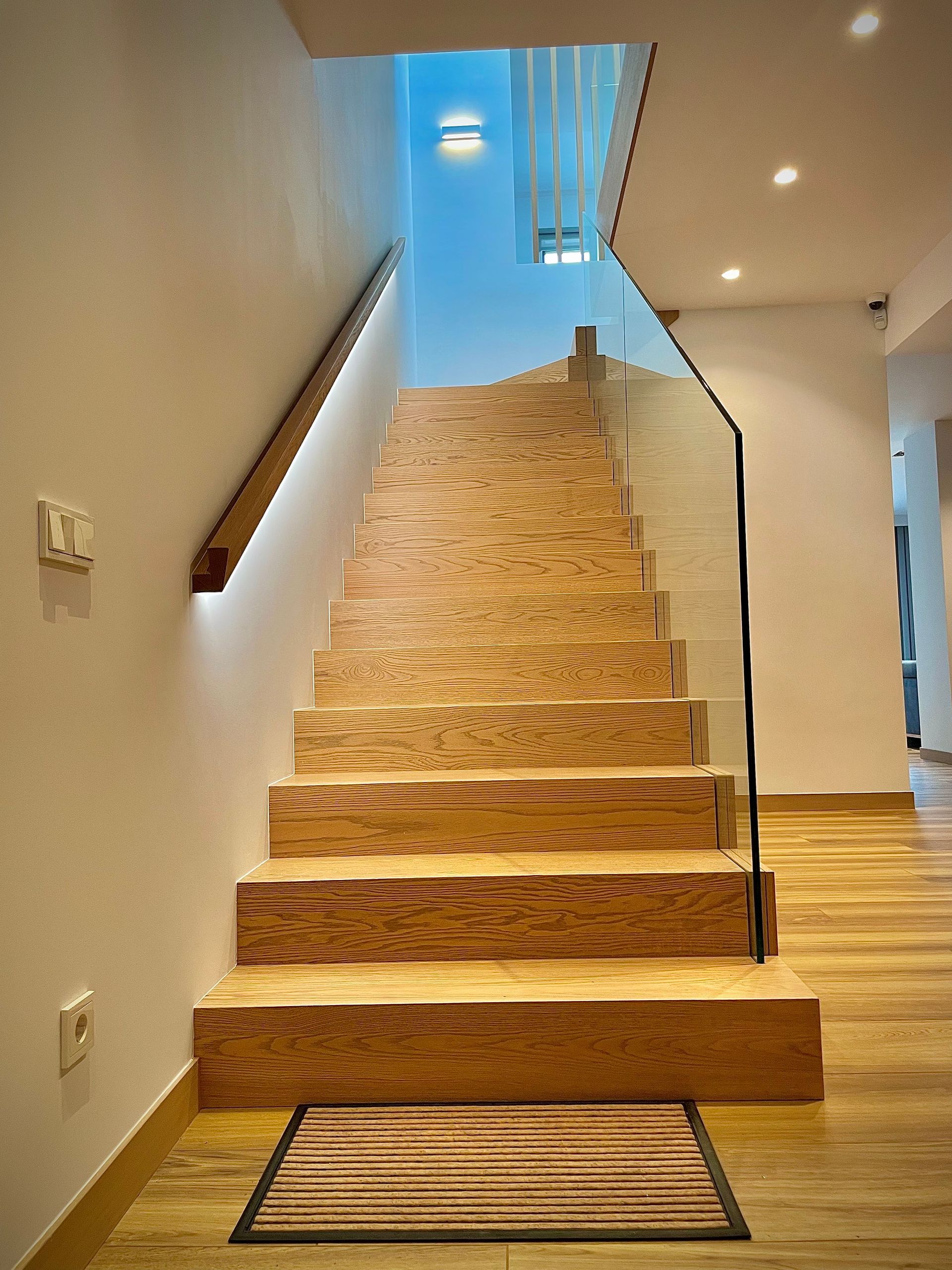 Una escalera con escalones de madera y barandilla de cristal.