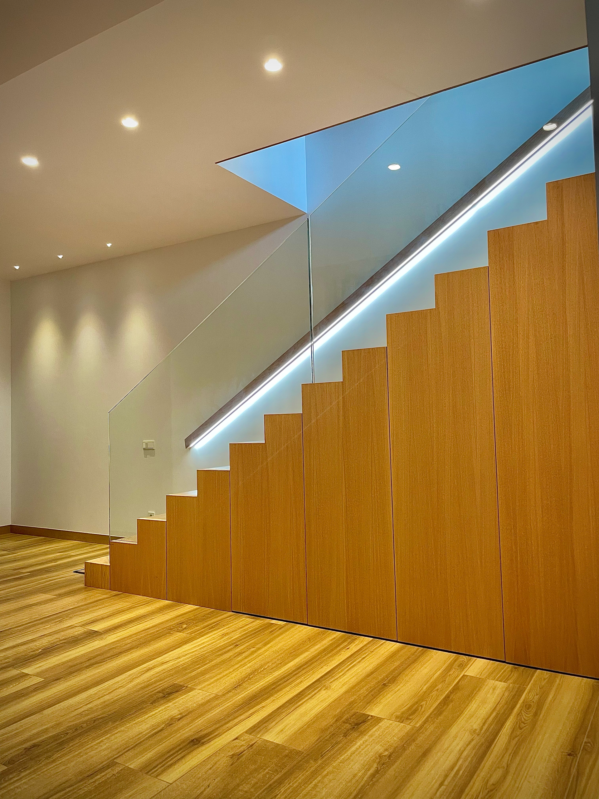 Una escalera de madera con barandilla de vidrio en una habitación.