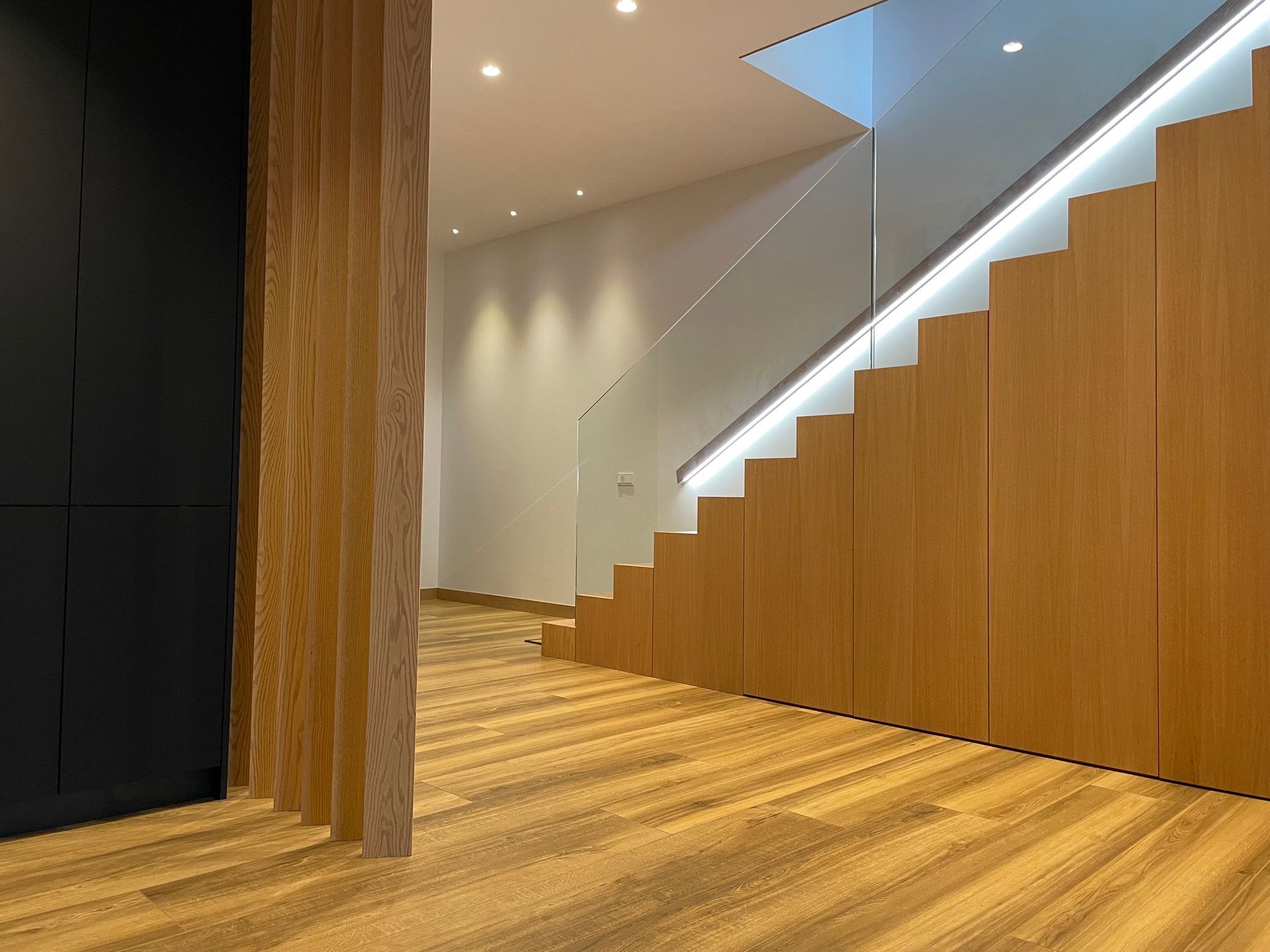 Una escalera de madera con barandilla de cristal en un pasillo.