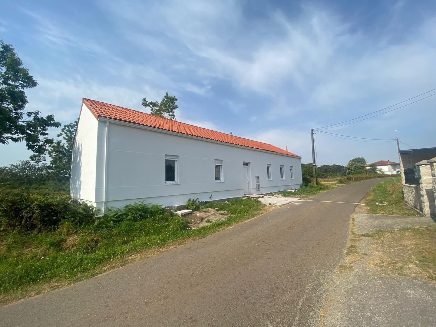 Una casa blanca con techo de tejas rojas está al costado de una carretera.