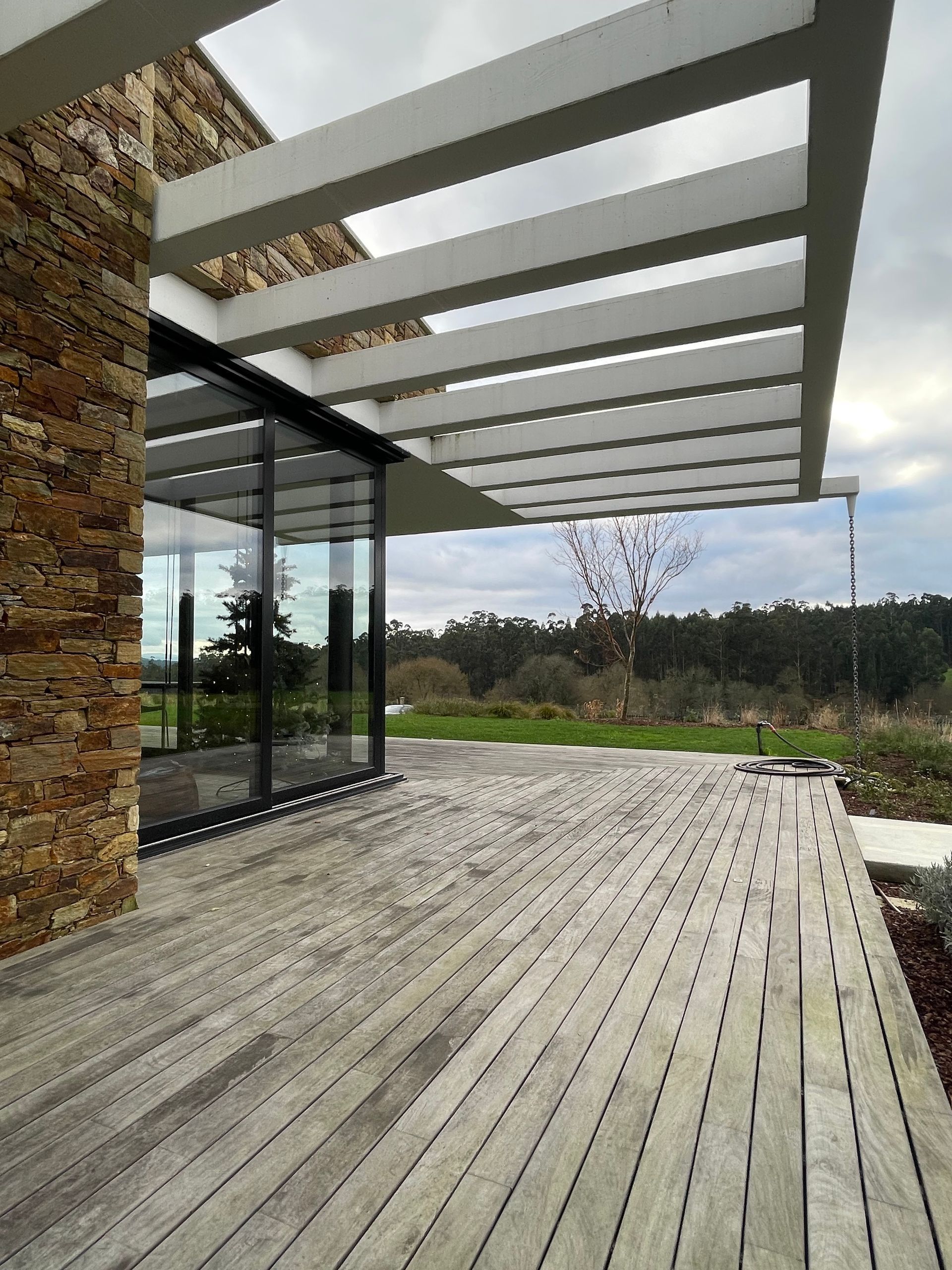 Una terraza de madera con una pérgola encima delante de una casa.