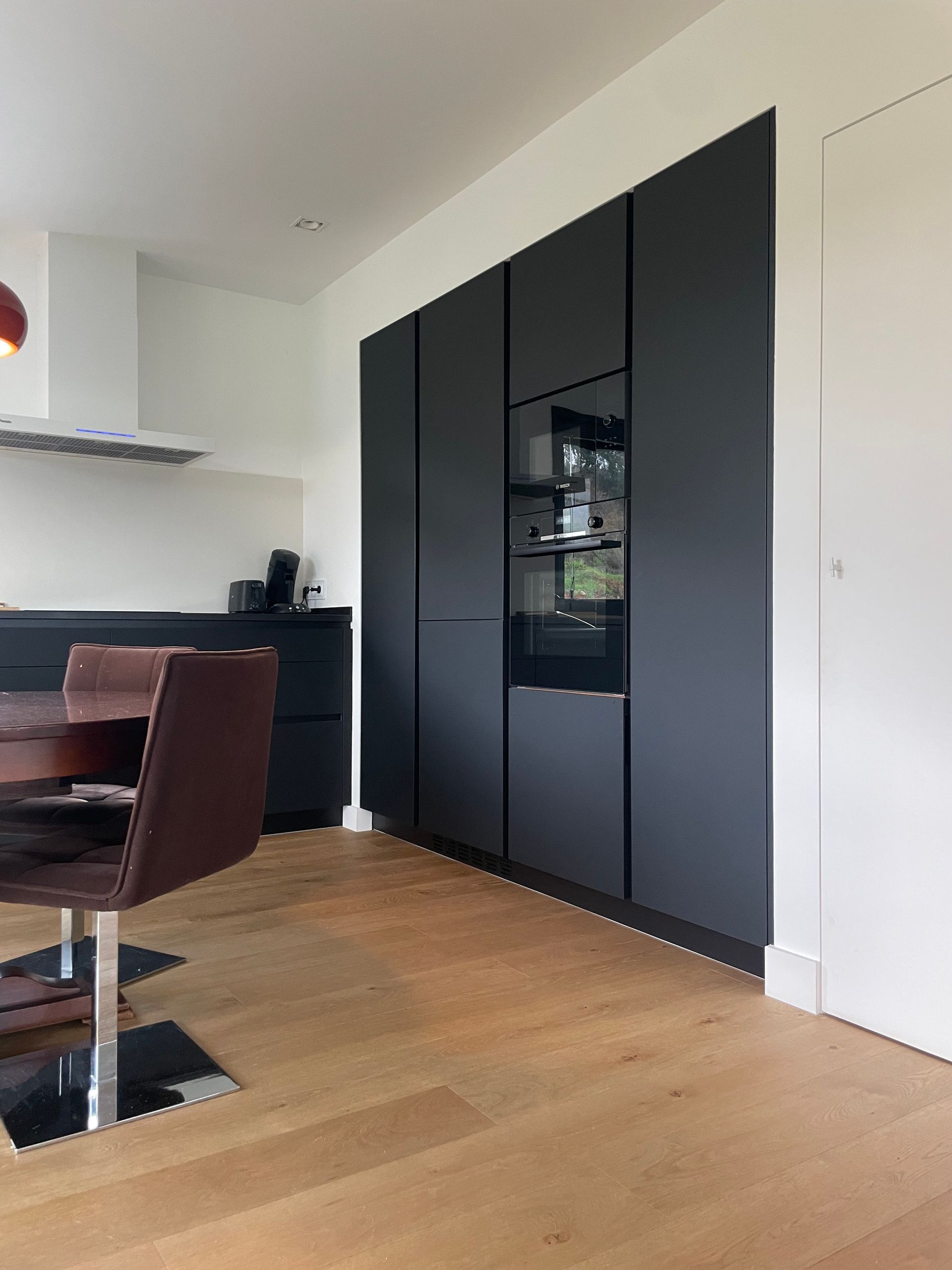 Una cocina con gabinetes negros y pisos de madera y una mesa y sillas.