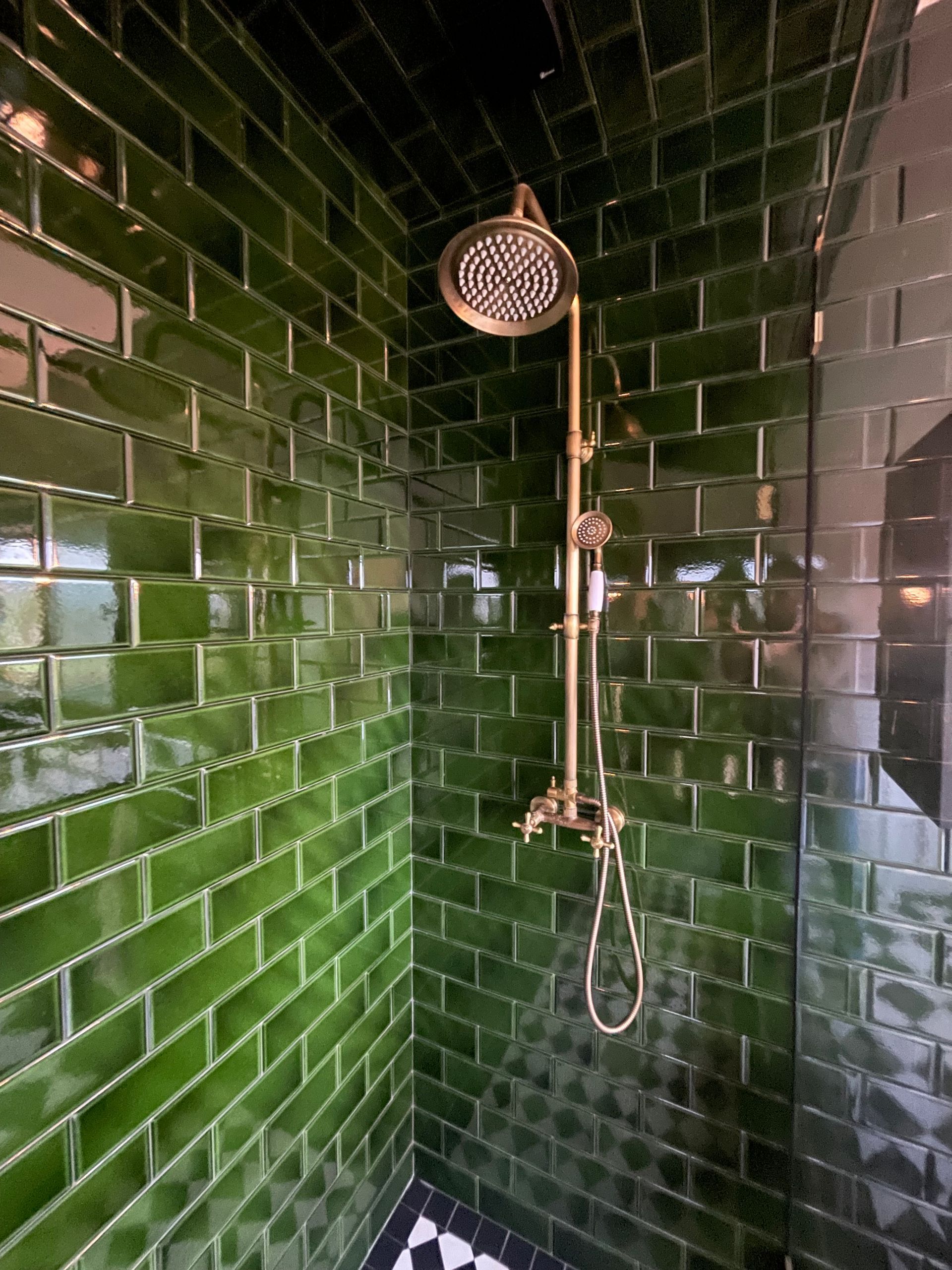 Una ducha con azulejos verdes y un cabezal de ducha de latón.