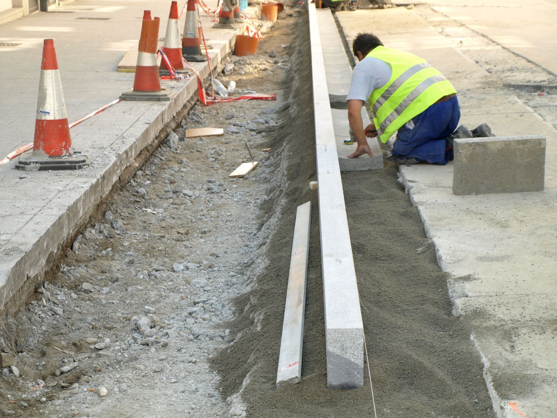 Un hombre con un chaleco amarillo está trabajando en una acera.