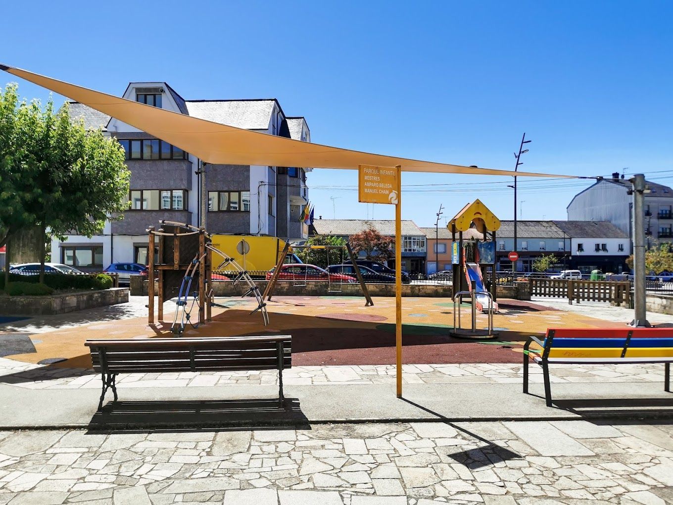 Un parque con una zona de juegos y un banco bajo un dosel.