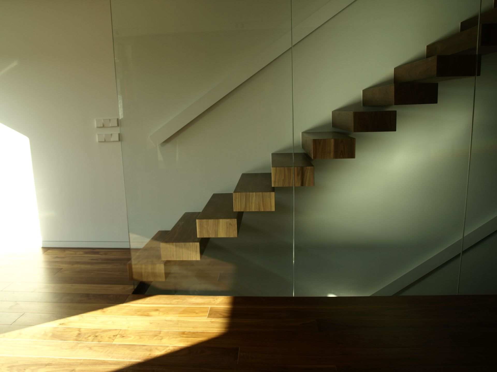 Una escalera con barandilla de cristal y escalones de madera.