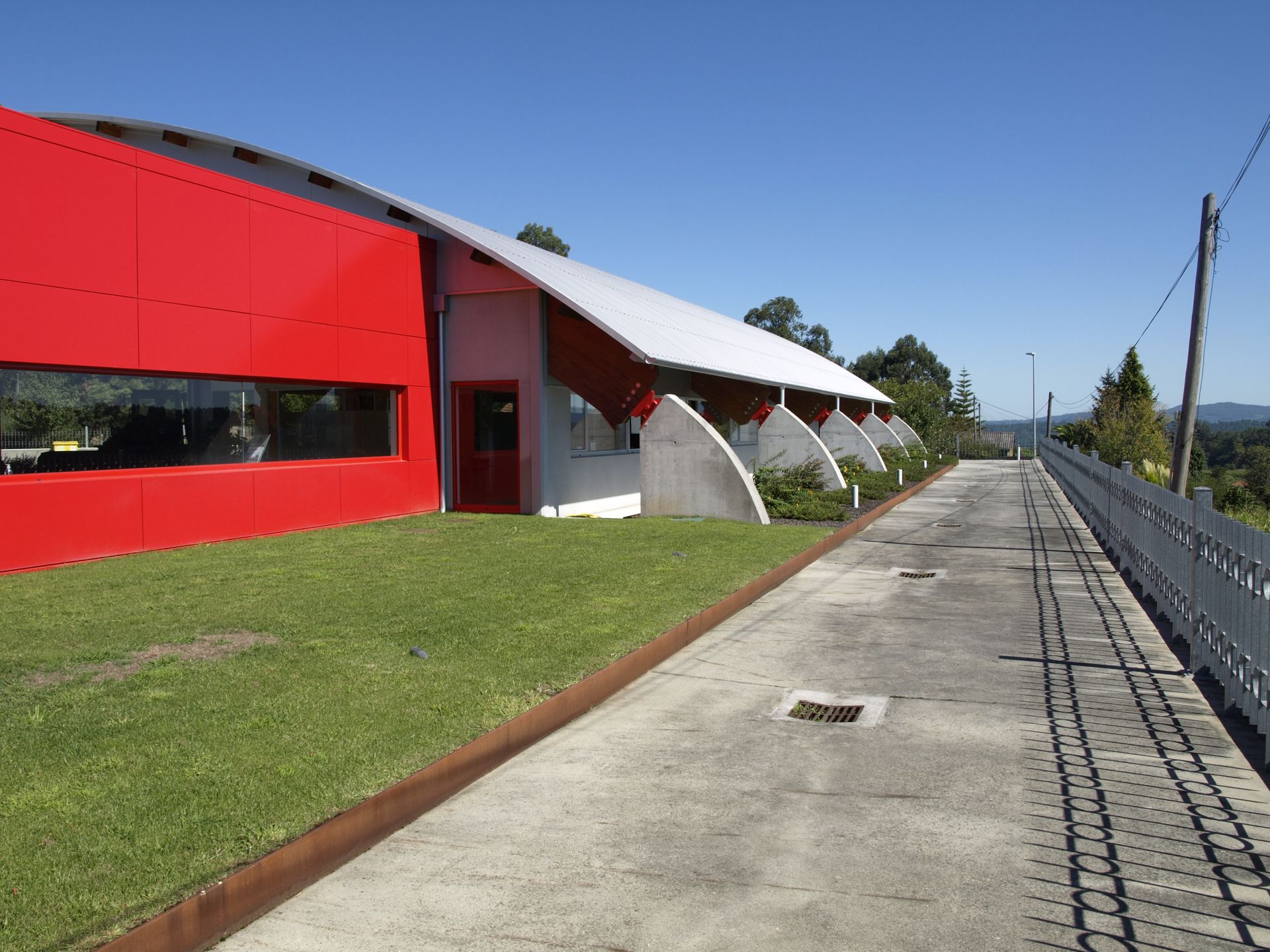Un edificio rojo con techo blanco está al lado de una pasarela de hormigón.