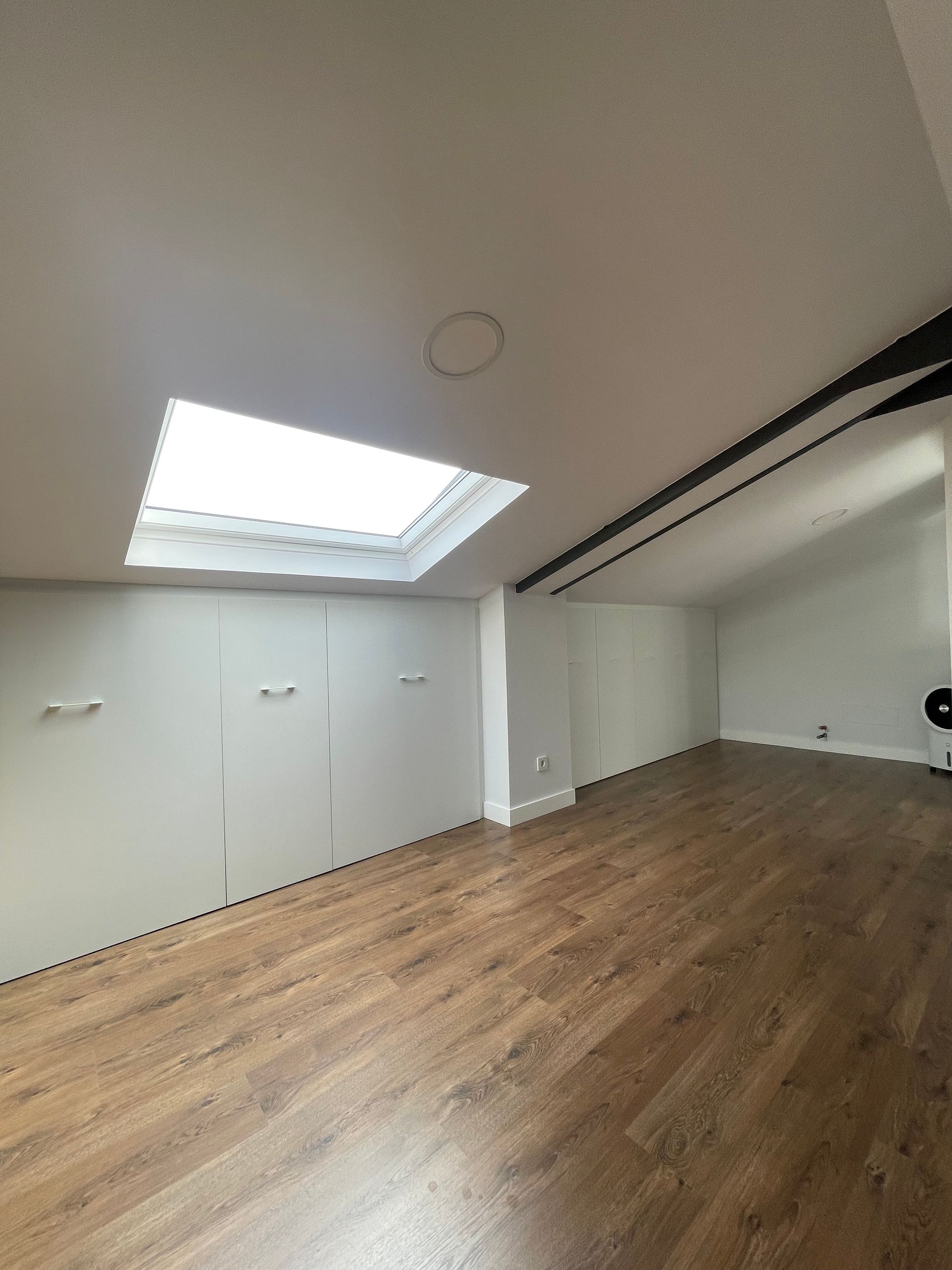 Una habitación vacía con pisos de madera y un tragaluz en el techo.