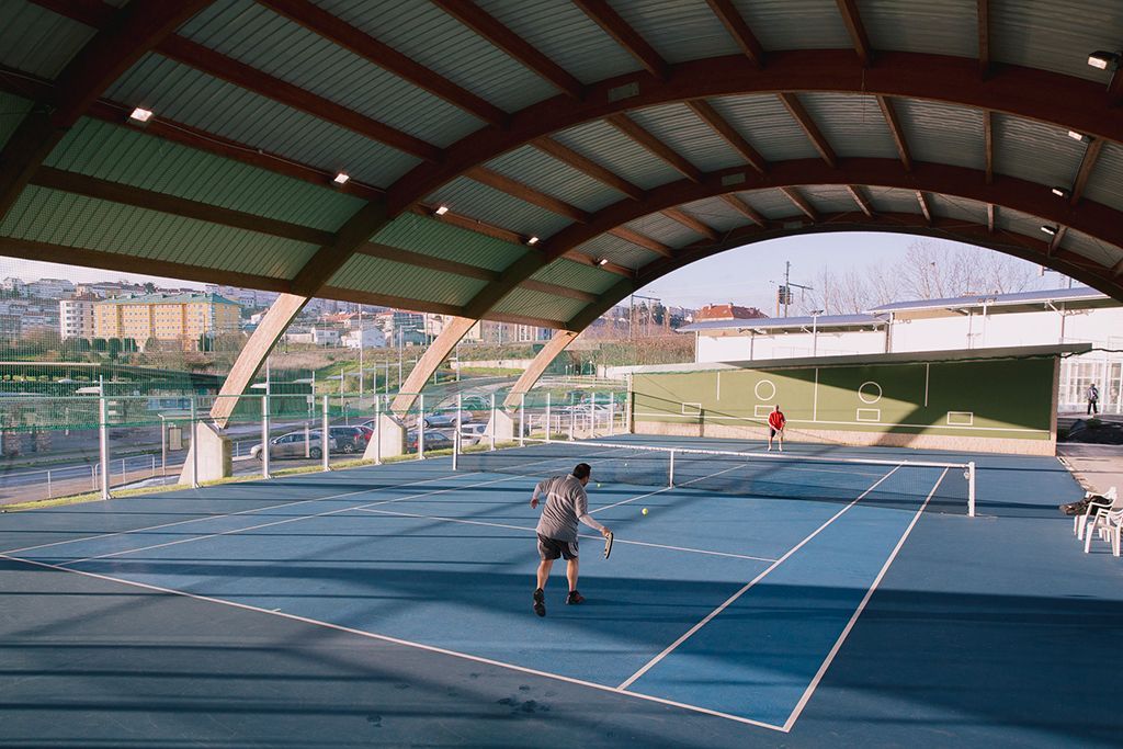 Un hombre está jugando al tenis en una cancha cubierta.
