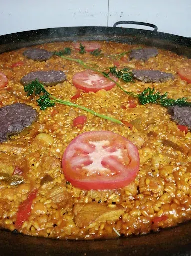 Una sartén grande llena de arroz, carne, tomates y perejil.