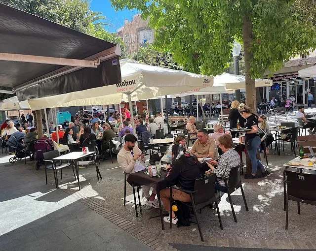 Un grupo de personas están sentadas en mesas bajo sombrillas en un restaurante.