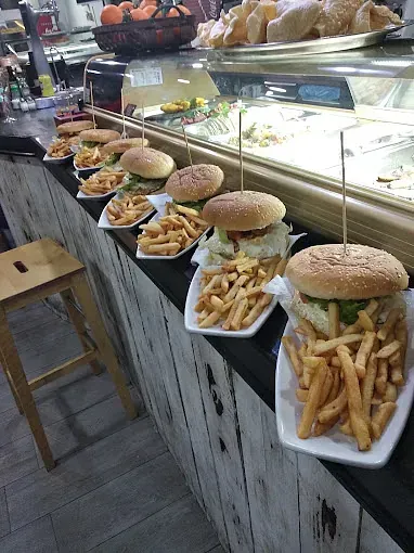 Una fila de hamburguesas y papas fritas en platos sobre un mostrador.
