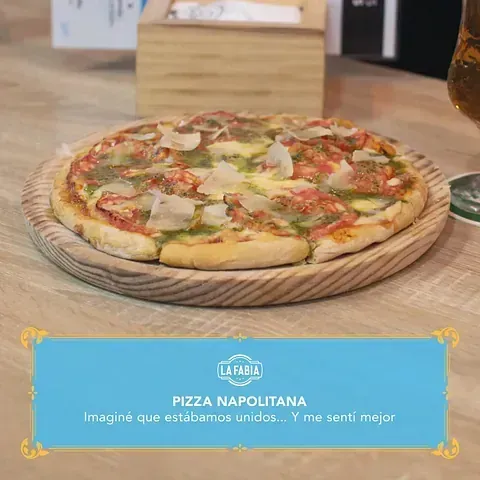 Pizza napolitana sobre una tabla de madera. Con salsa roja, pesto verde y parmesano rallado. Texto superpuesto: «La Fabia» y una cita.