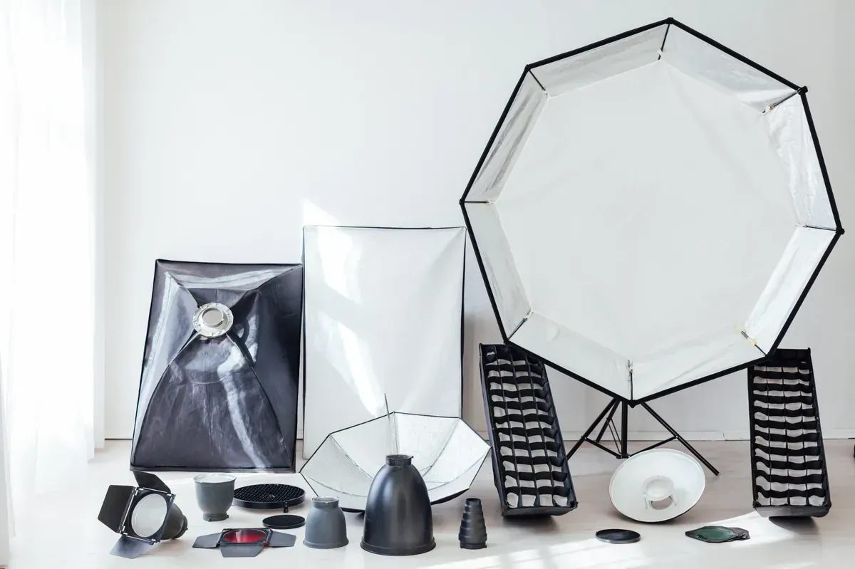 Equipo de iluminación de estudio sobre un piso blanco contra una pared blanca; incluye softboxes.