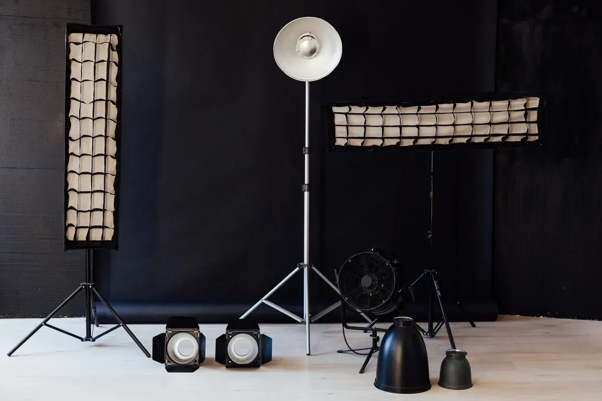 Equipo de iluminación de estudio sobre fondo negro: softboxes, reflectores, focos y soportes.