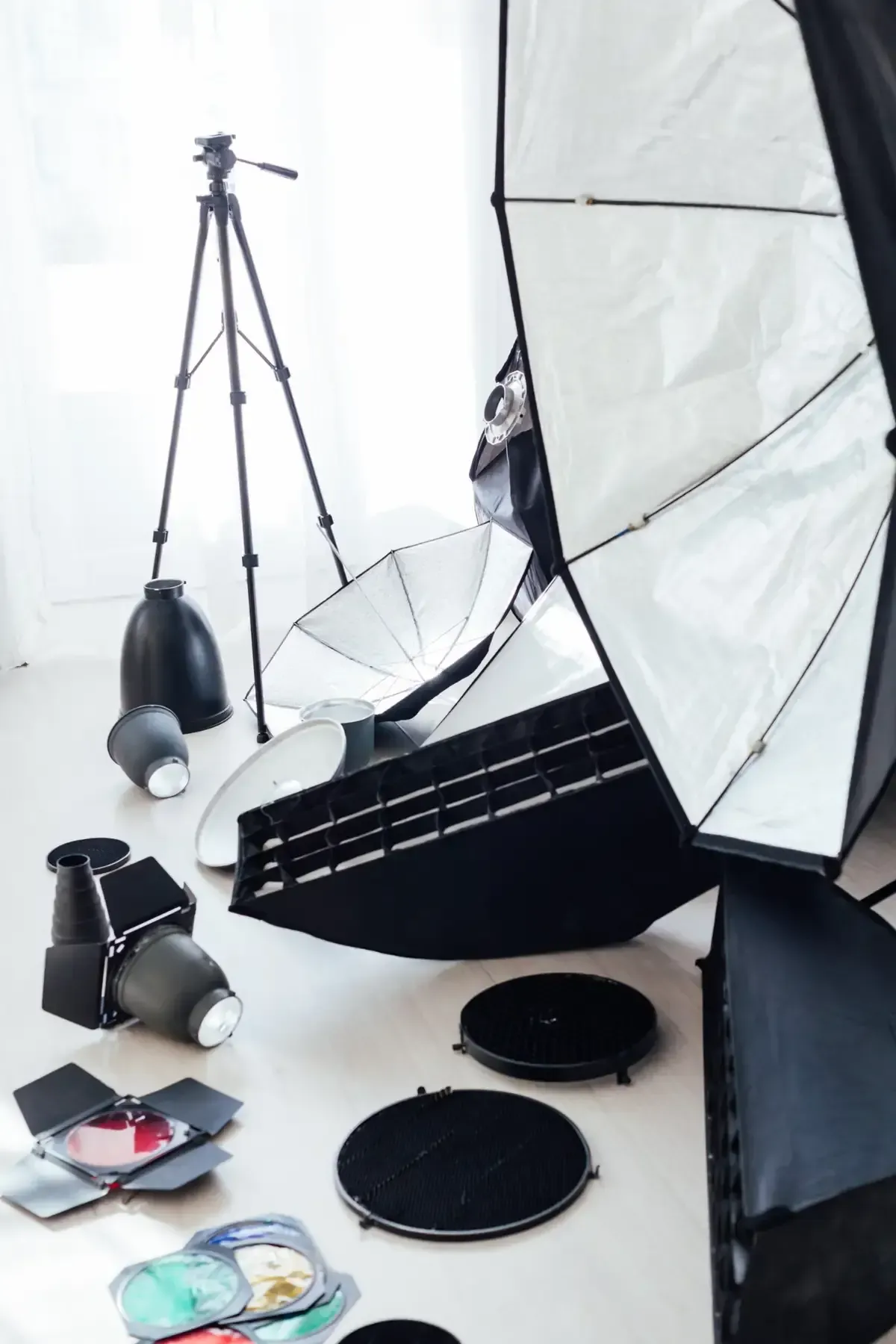 Equipo de fotografía en un estudio blanco: trípode, reflectores, softboxes y luces.