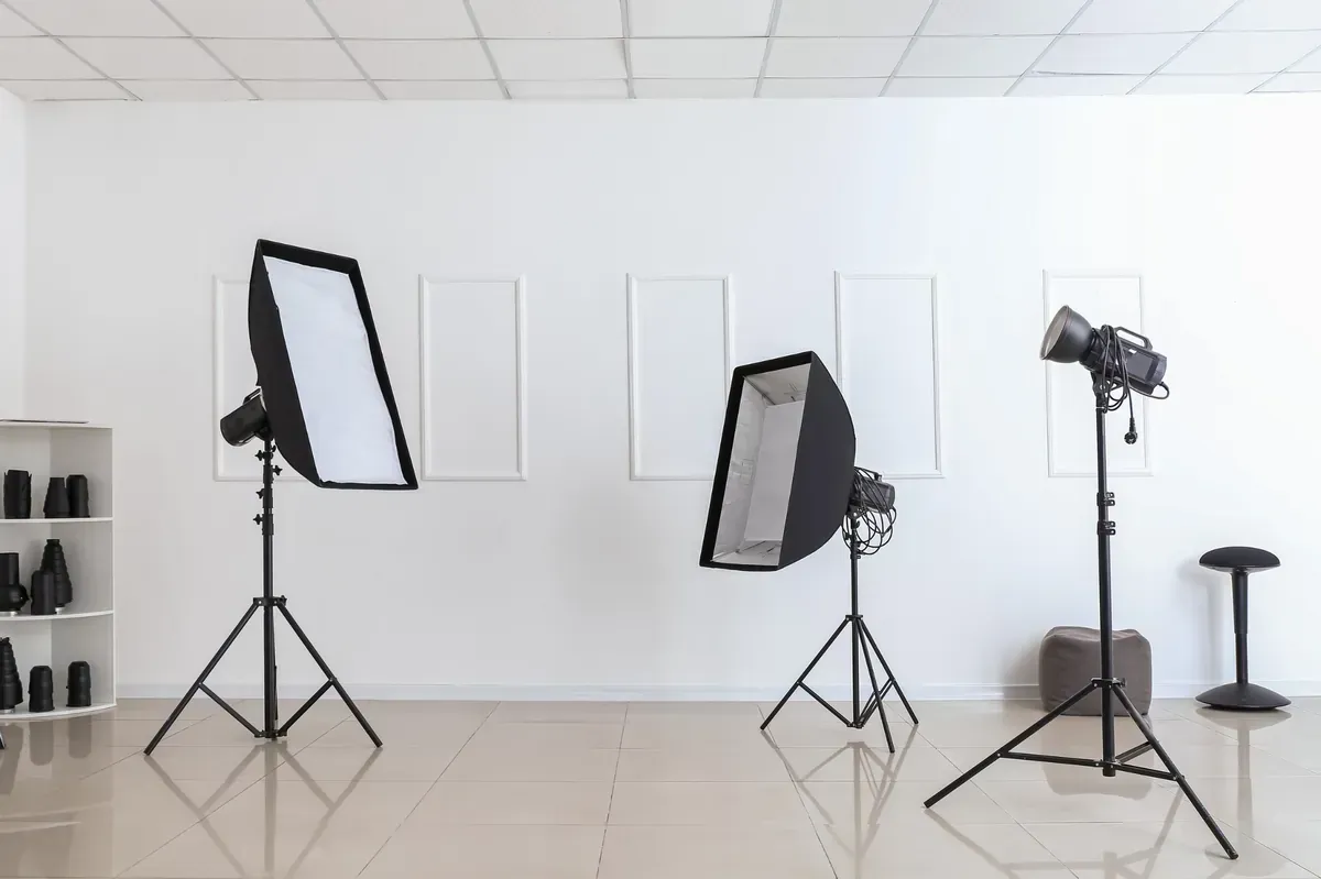Estudio de fotografía con tres luces sobre soportes, paredes blancas y tres marcos vacíos.