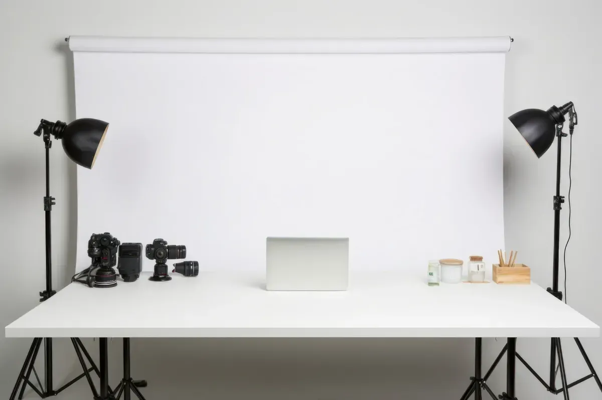 Estudio fotográfico con fondo blanco, mesa, luces, cámaras, computadora portátil y accesorios.