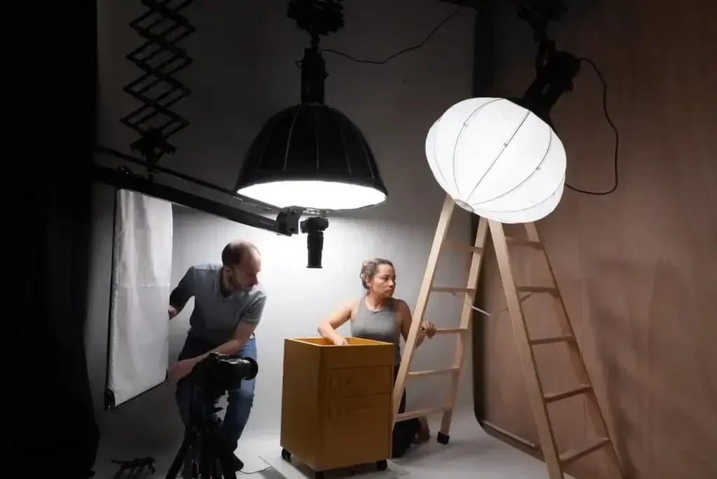 Personas en un estudio con equipo de iluminación, ajustando las luces. Una persona en una escalera.