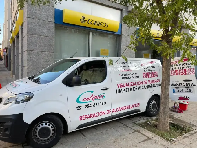 Una furgoneta de reparto blanca aparcada frente a un edificio de correos amarillo y blanco.