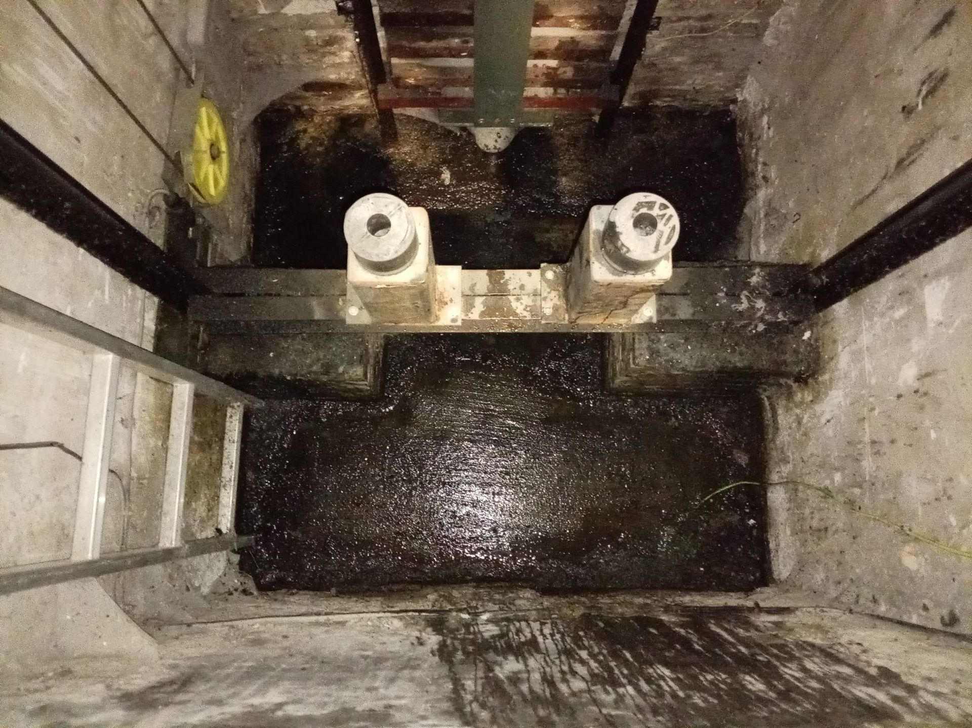 En el interior de un pozo de hormigón, dos accesorios de tubería blancos se sitúan sobre un lavabo oscuro y húmedo.