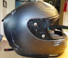 Ein zerkratzter schwarzer Motorradhelm, der auf einem Tisch liegt.