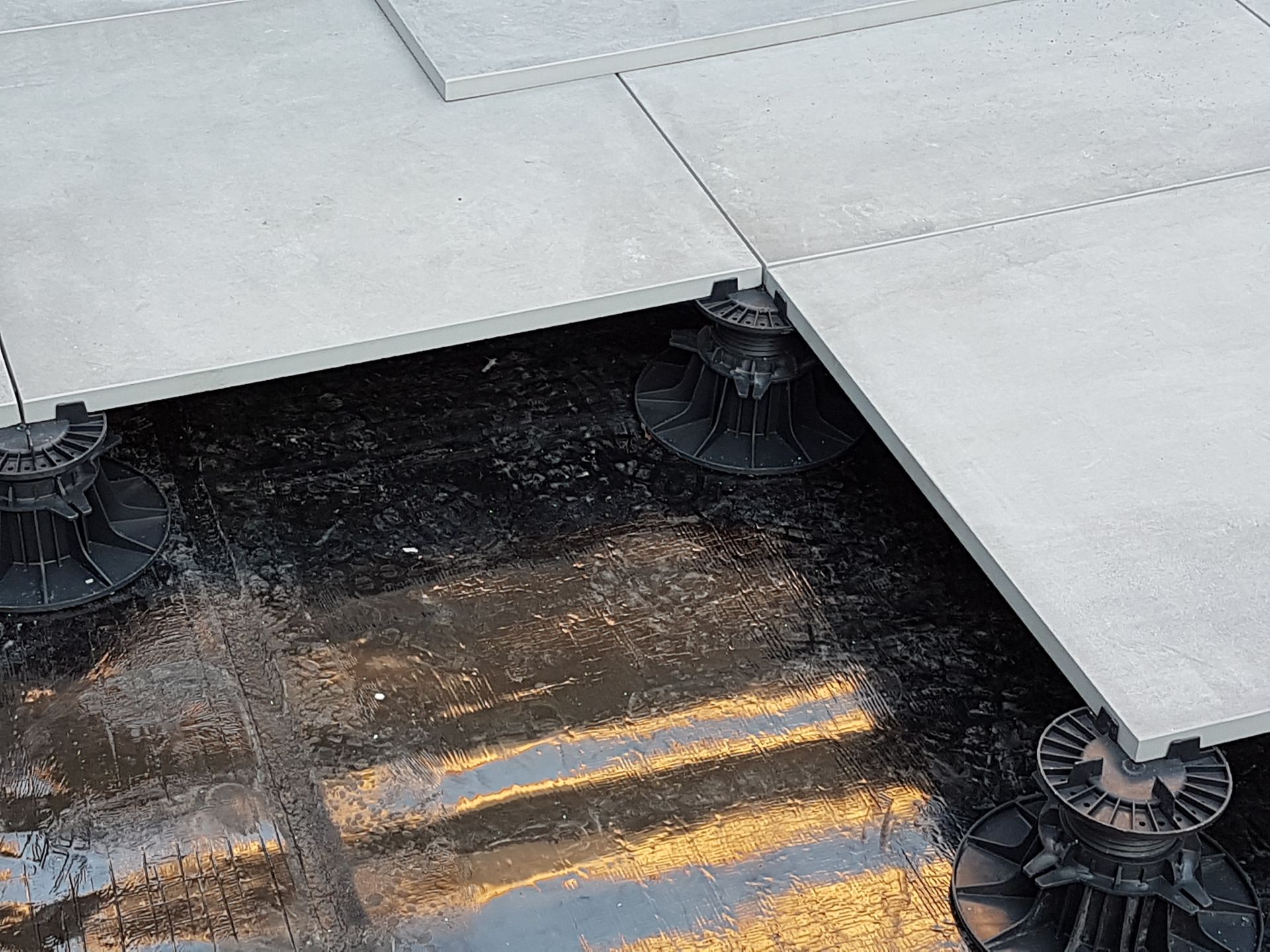 Tuiles de toiture grises sur supports à plots réglables, reposant sur une membrane d'étanchéité noire aux reflets jaunes.