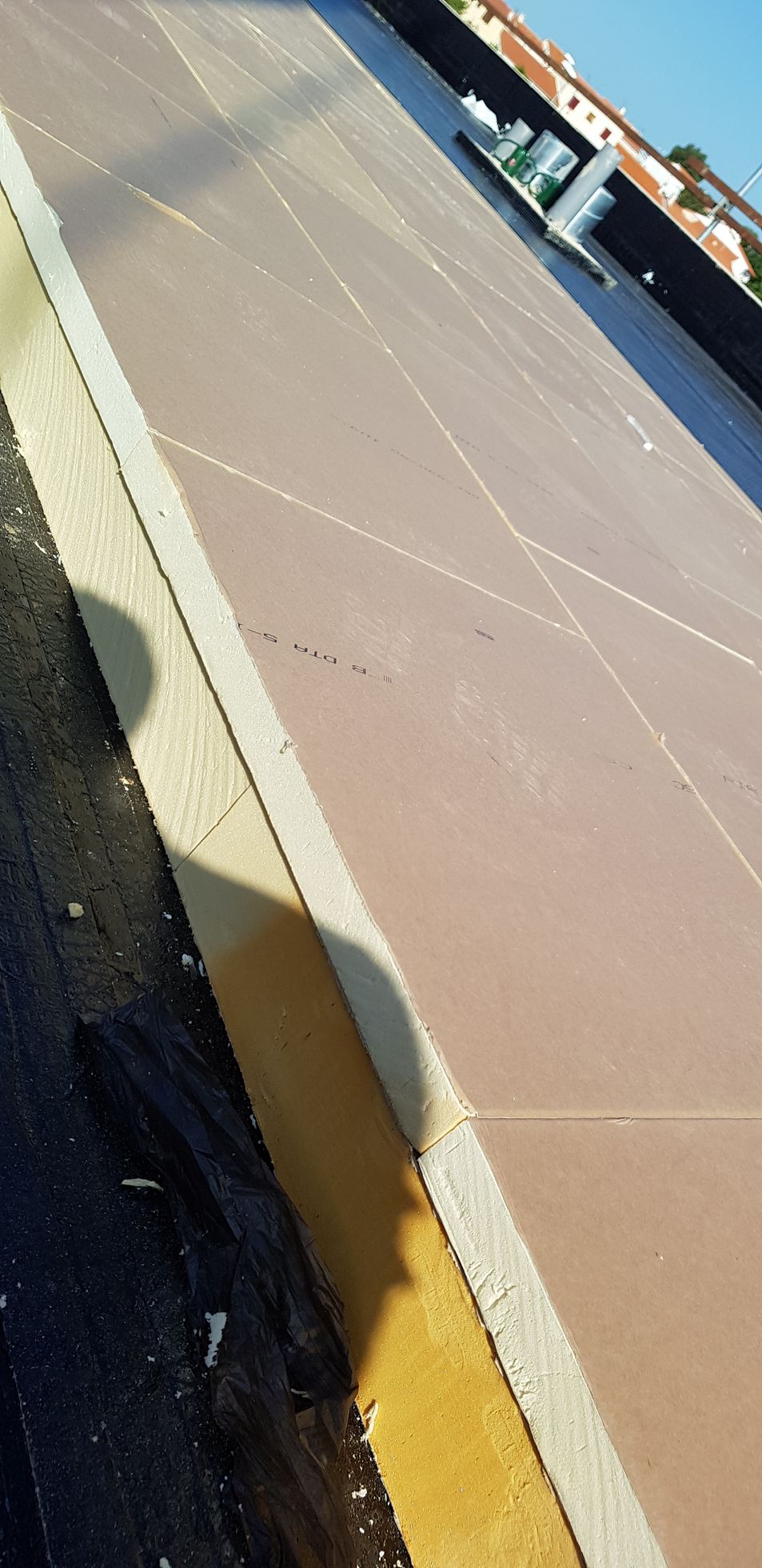 Vue inclinée d'un toit à la surface beige, aux bords jaunes, avec des bâtiments au loin.