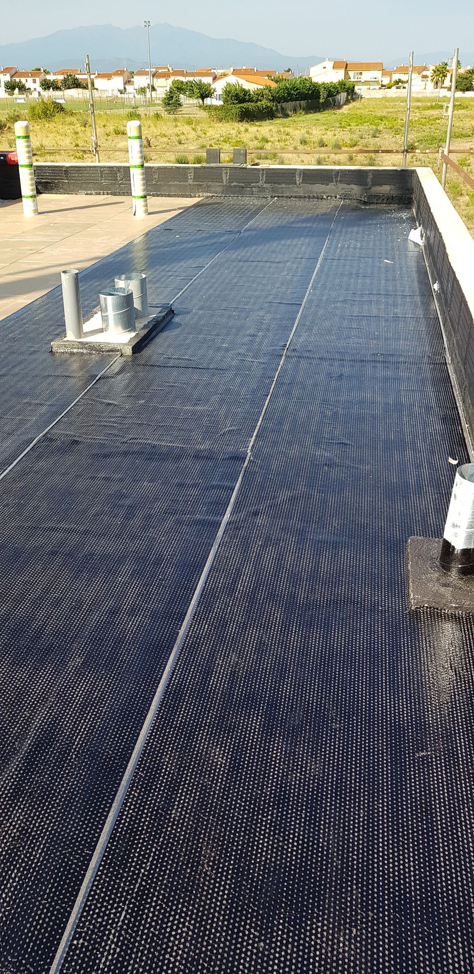 Sous-couche de toiture recouverte d'une membrane d'étanchéité noire et raccords de tuyauterie exposés au soleil
