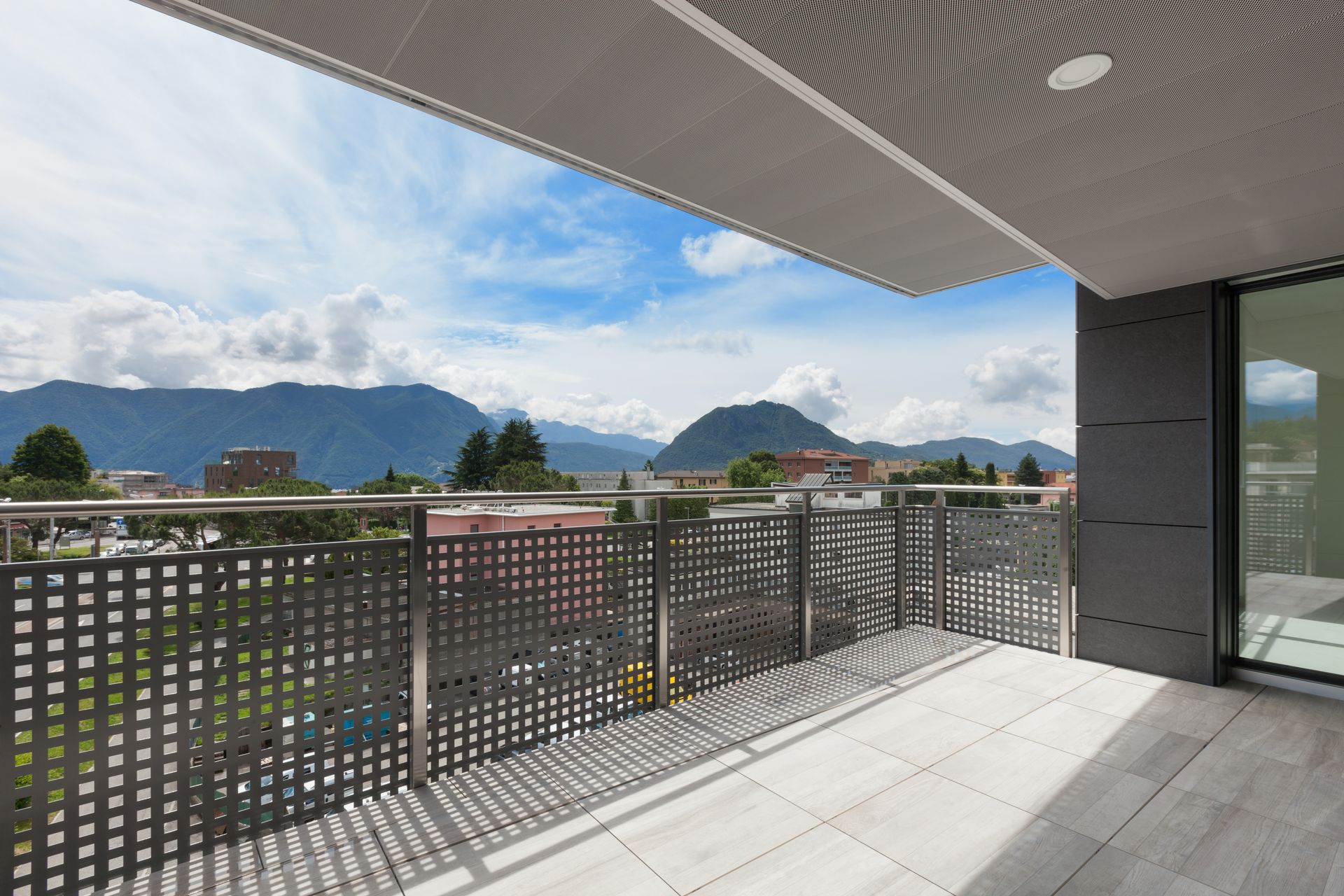Balcon moderne avec sol carrelé, rambarde perforée et vue sur la montagne sous un ciel nuageux