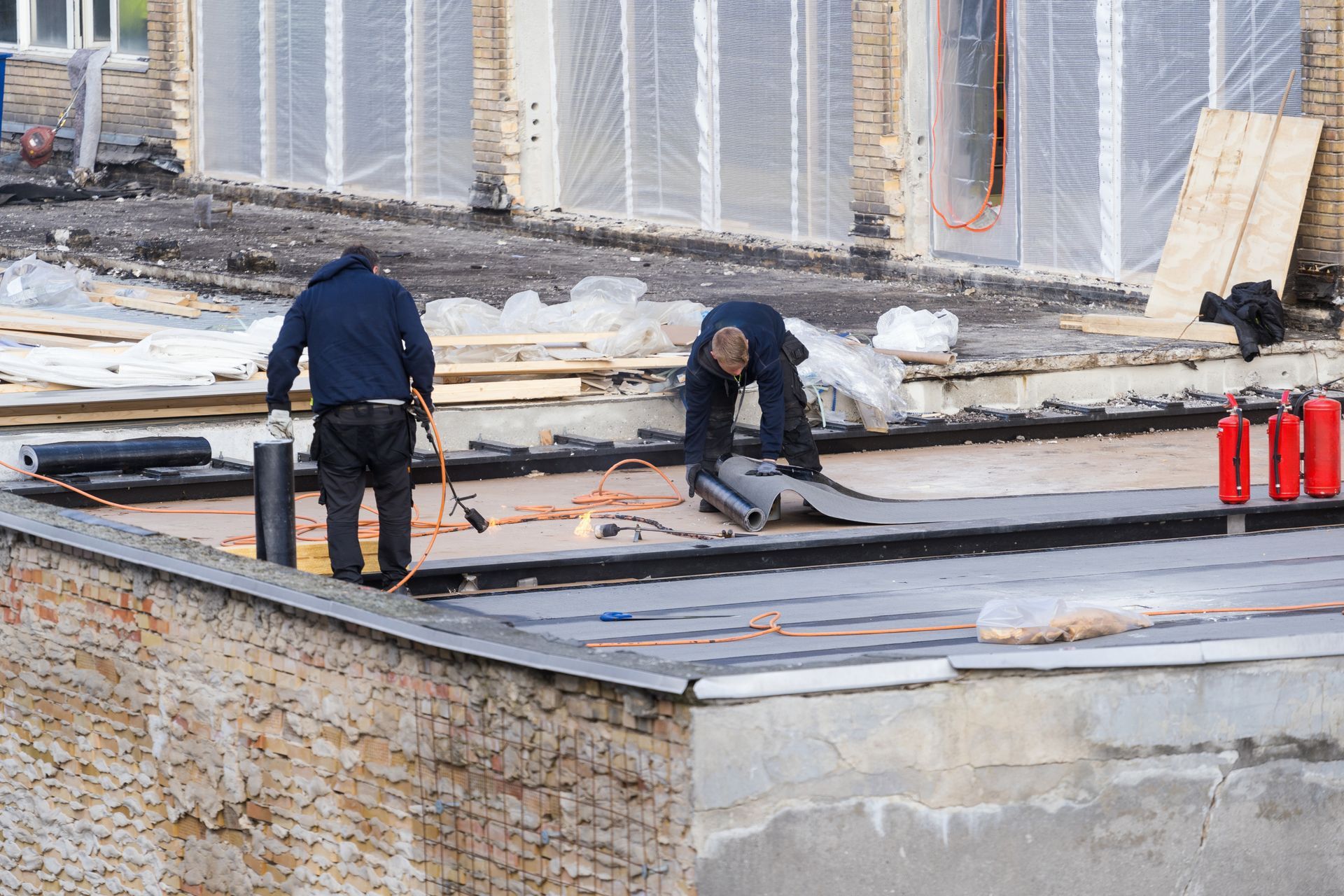 Deux ouvriers travaillent sur un toit en train d'imperméabiliser un toit plat près d'un parapet en béton.