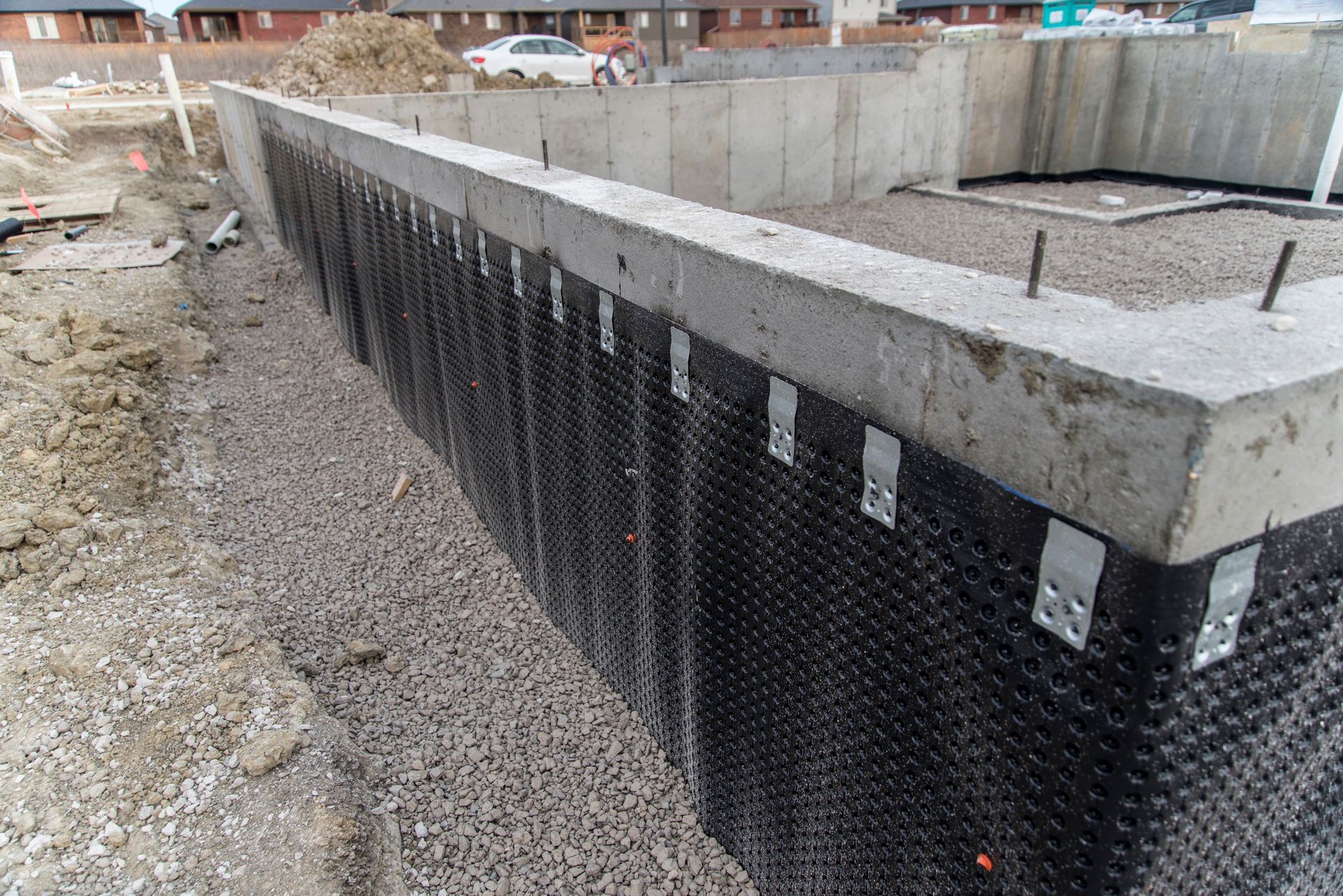 Mur de fondation avec membrane d'étanchéité noire et tranchée de drainage en gravier