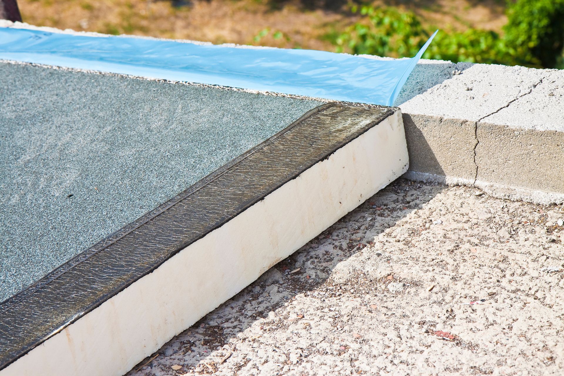 Rampe d'accès en béton rejoignant un trottoir pavé de bleu et de gris avec un bord engazonné
