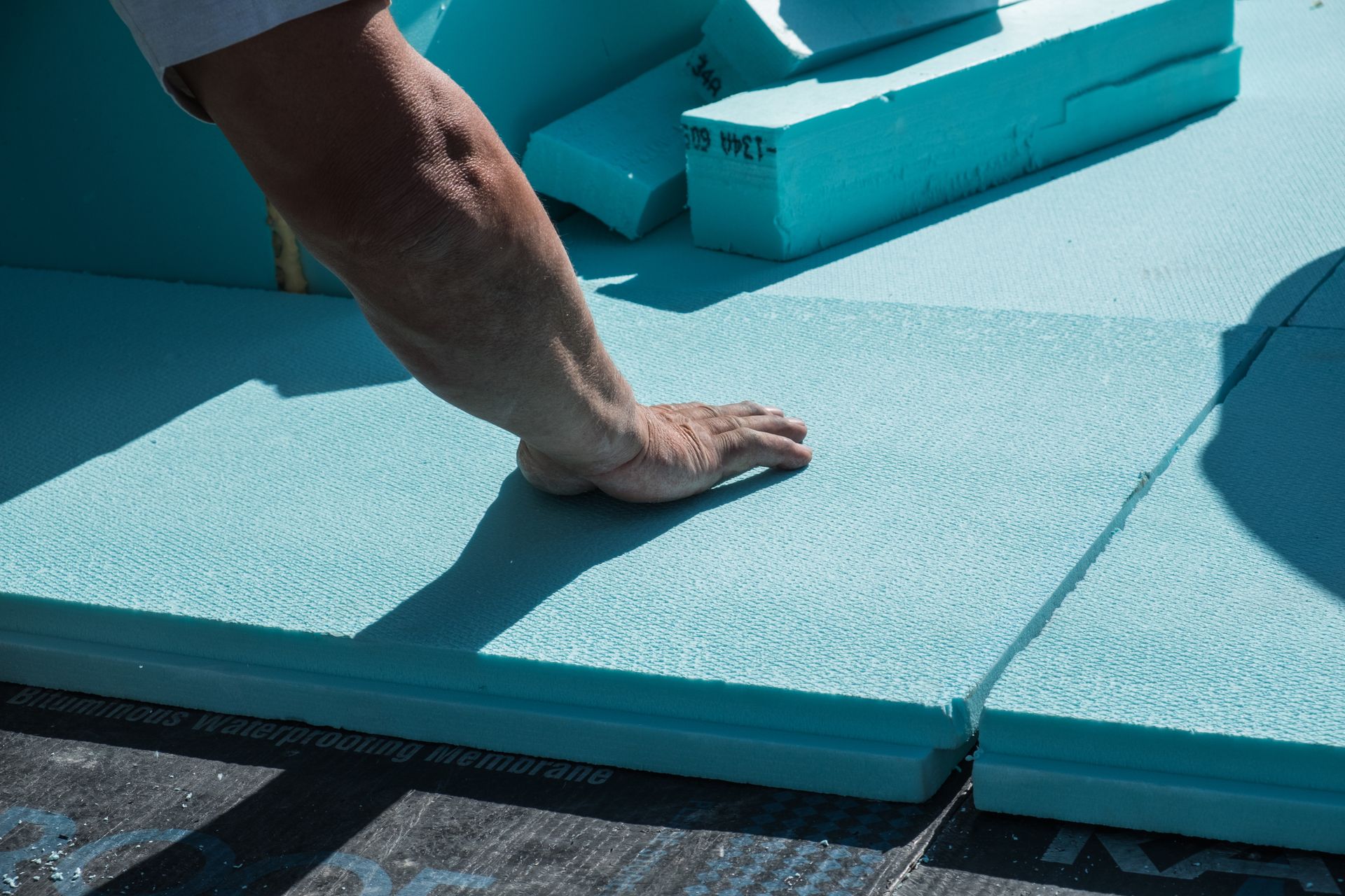 Personne posant des panneaux d'isolation en mousse bleue sur un toit en construction
